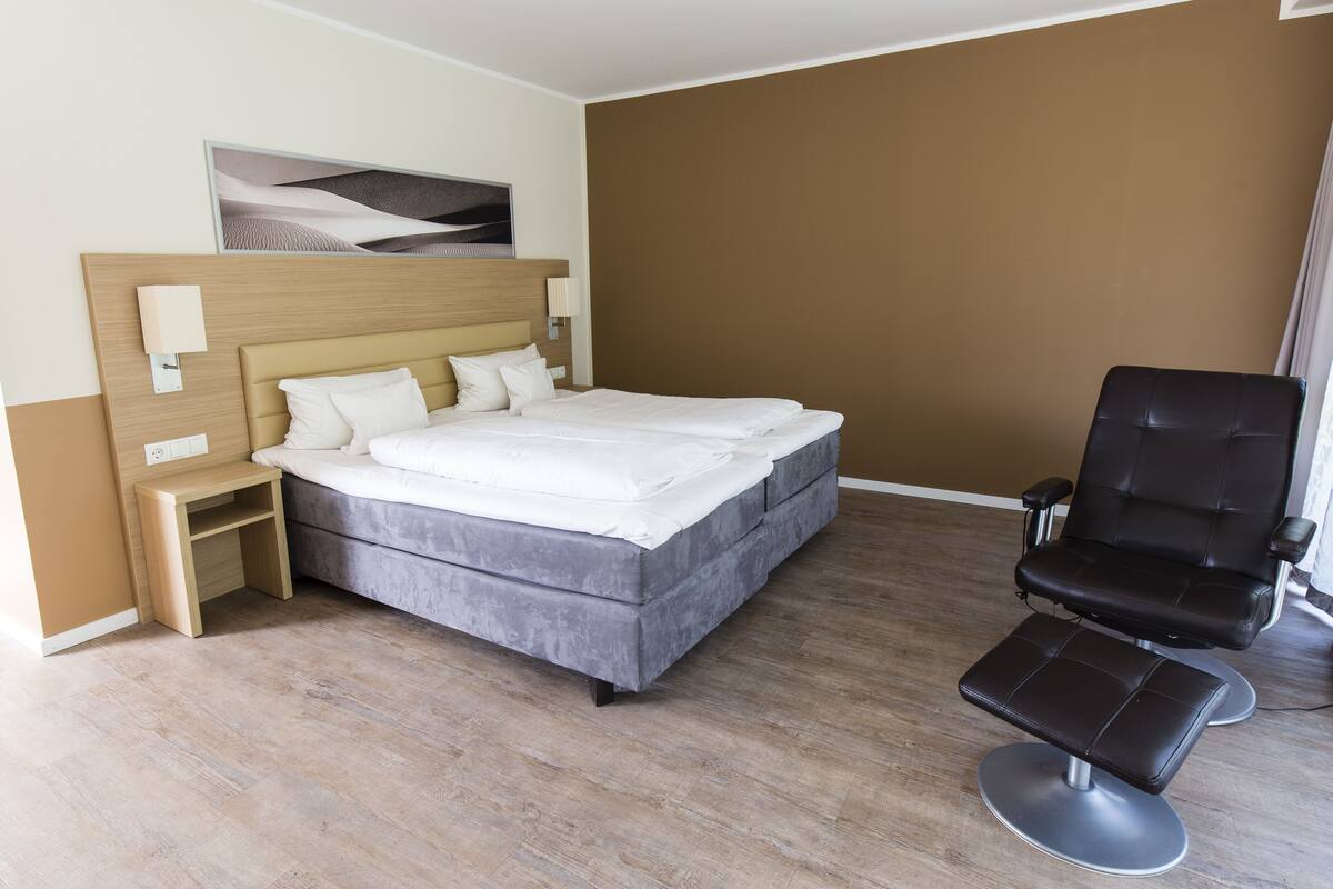 Una habitación de hotel con cama, mesita de noche, silla y un cuadro en la pared.