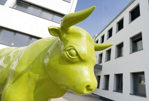A bright green cow sculpture in front of a modern building with multiple windows. - BONNOX Boardinghouse & Hotel (Bonn)