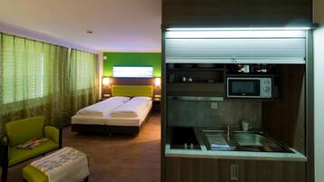A hotel room with a bed, a chair, a small table, and a kitchenette with a microwave and sink.
