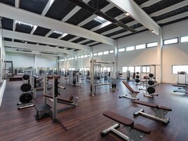 A spacious gym with various exercise equipment, large windows, and a high ceiling.