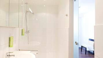 Un baño moderno con un lavamanos grande de color blanco, una ducha y una puerta de cristal que da a un dormitorio.