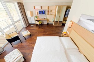 A hotel room with a bed, a desk, a chair, a TV, and a wardrobe.