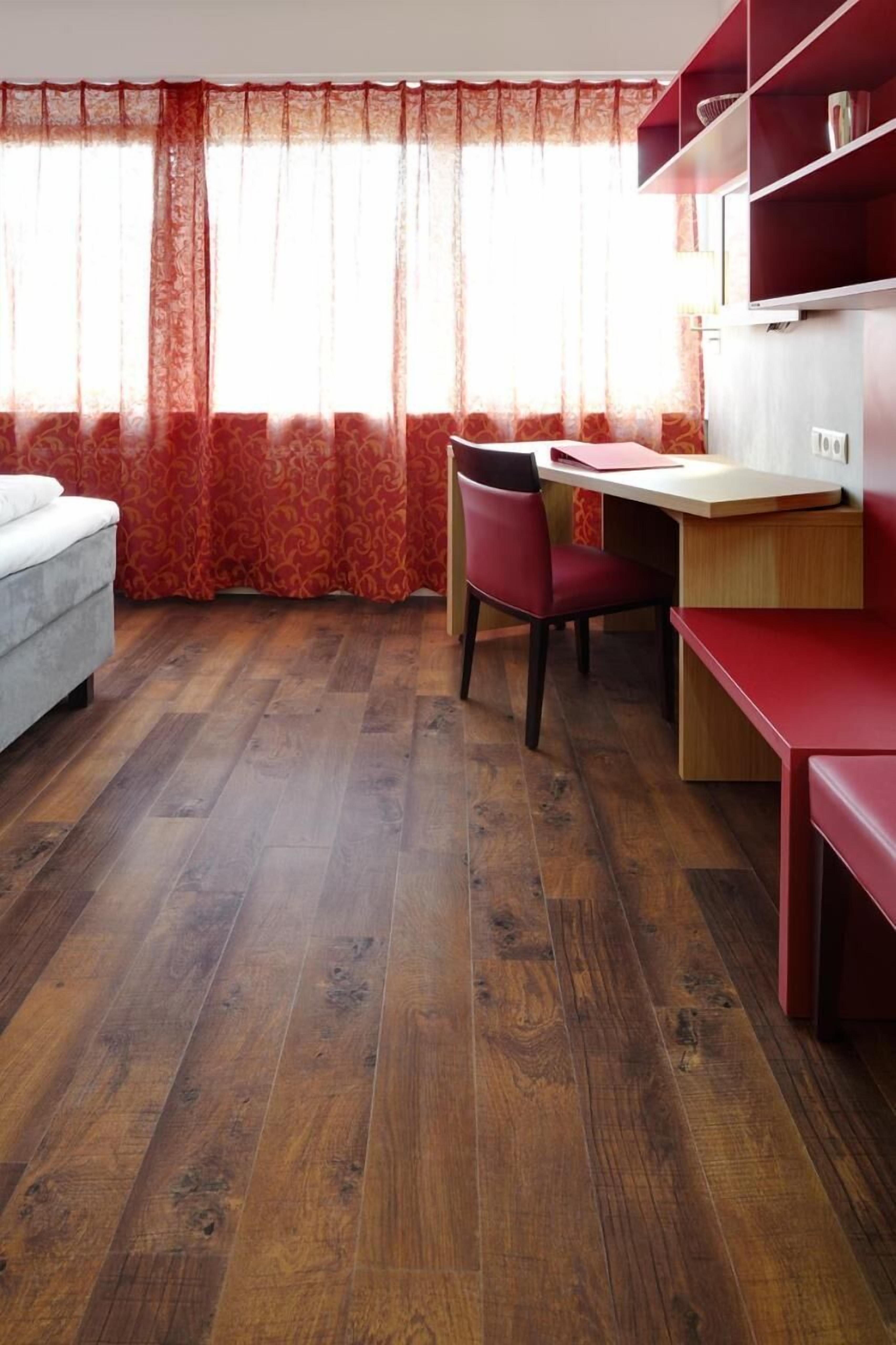 Una habitación con piso de madera, un escritorio con silla, una estantería roja y una ventana con cortinas rojas.