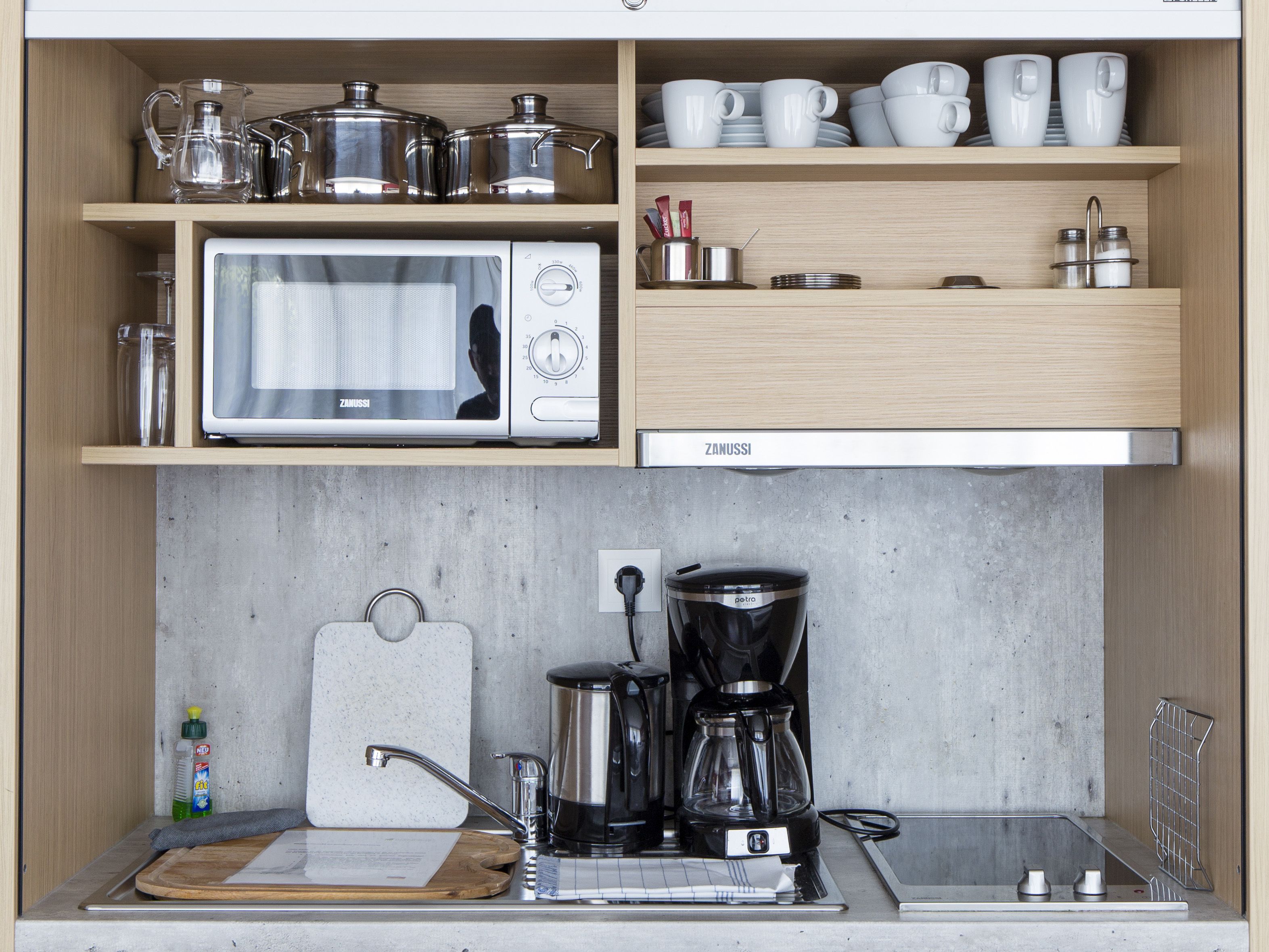 Een kleine keuken met een inbouwmagnetron, koffiezetapparaat en een klein spoelgedeelte.