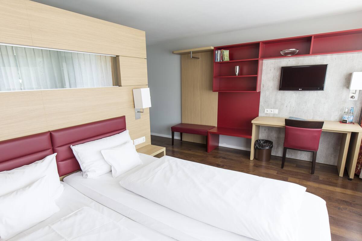 Habitación de hotel con una cama grande, un escritorio, un televisor y una estantería.