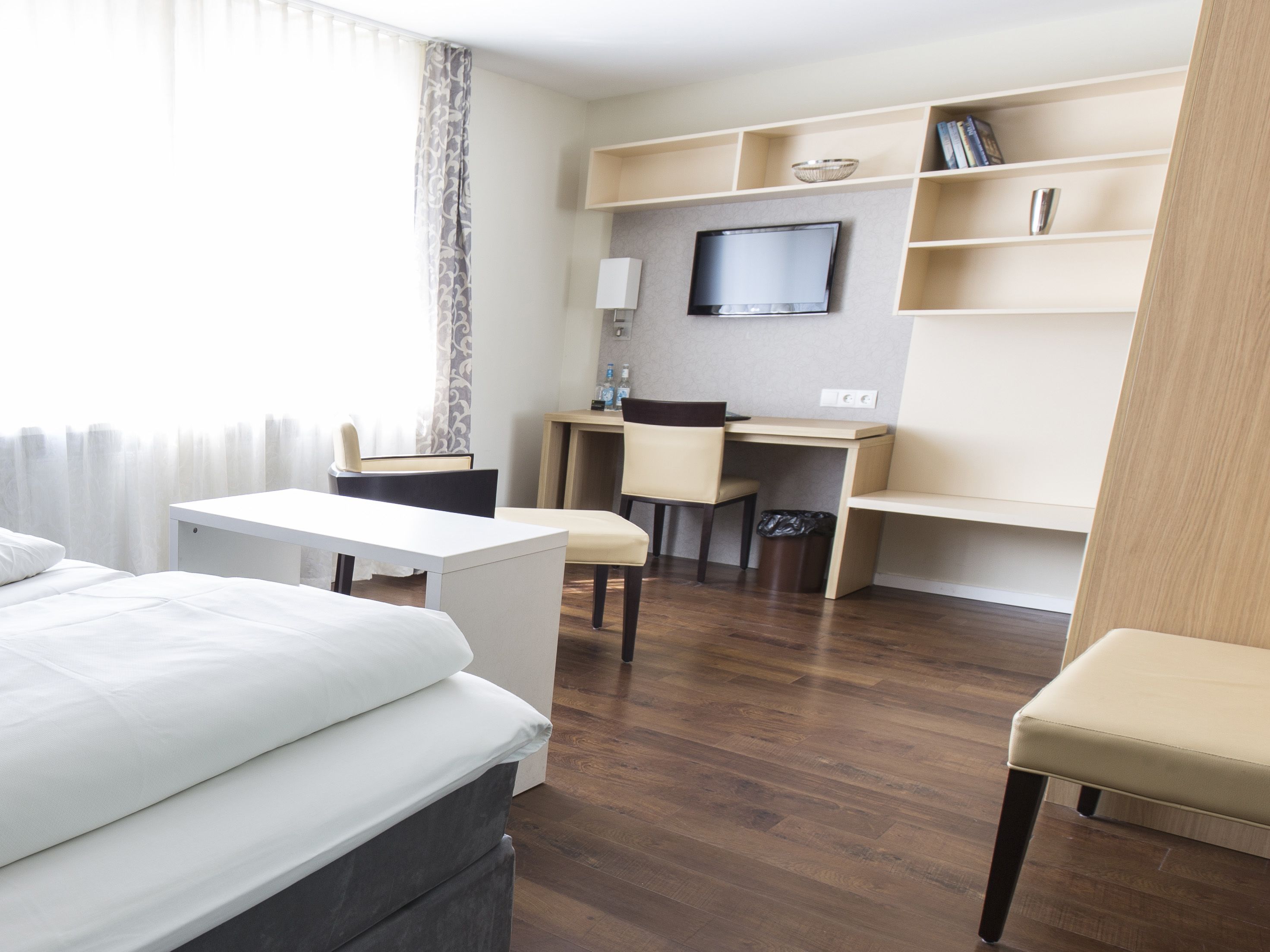 A hotel room with a bed, a desk, a chair, a TV, and a bookshelf.