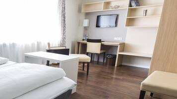 A hotel room with a bed, a desk, a chair, a TV, and a bookshelf.