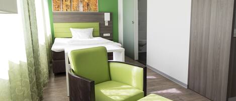 Habitación de hotel con cama, una silla, un banco, un cuadro en la pared y una puerta corrediza.