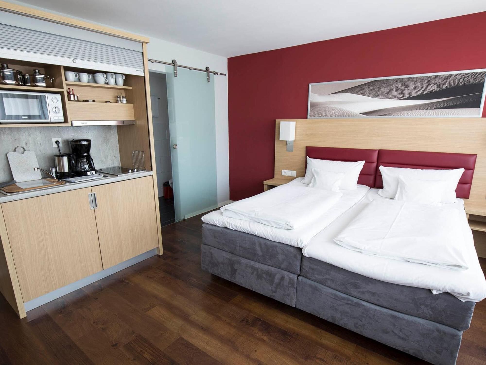 Ein Hotelzimmer mit Bett, einer Küchenzeile und einer roten Akzentwand.