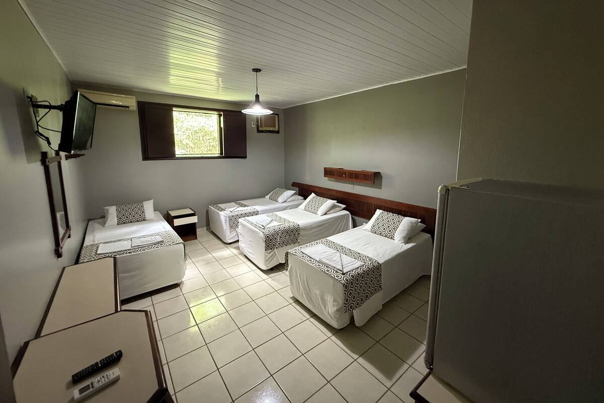 Une chambre d’hôtel avec deux lits simples, une télévision, une petite table et une fenêtre avec des stores.