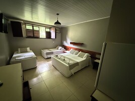 Una habitación de hotel compacta con dos camas individuales, un sofá cama, una mesita y un refrigerador.