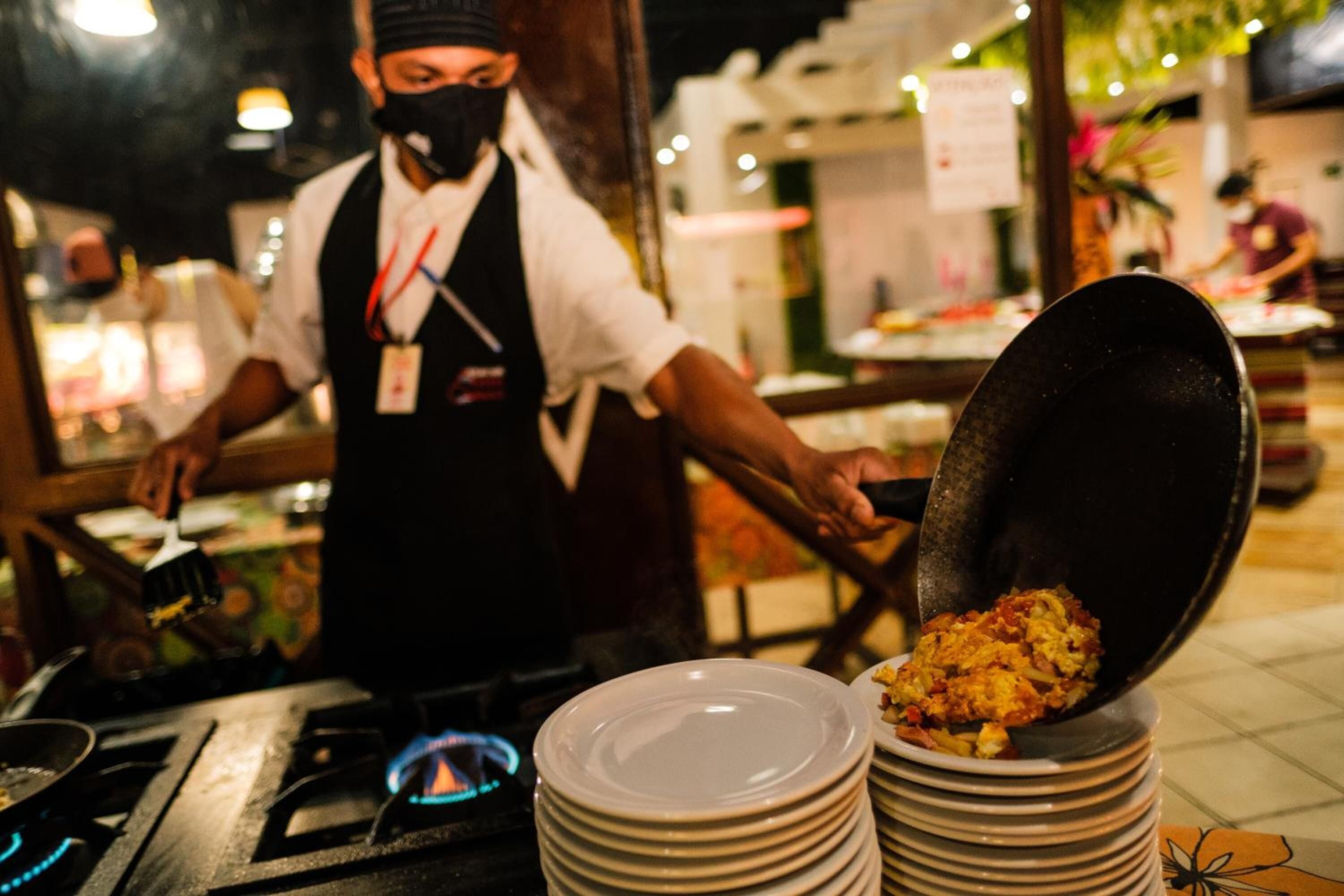 Una cocina de restaurante con un chef preparando comida, una pila de platos y un wok sobre una estufa.