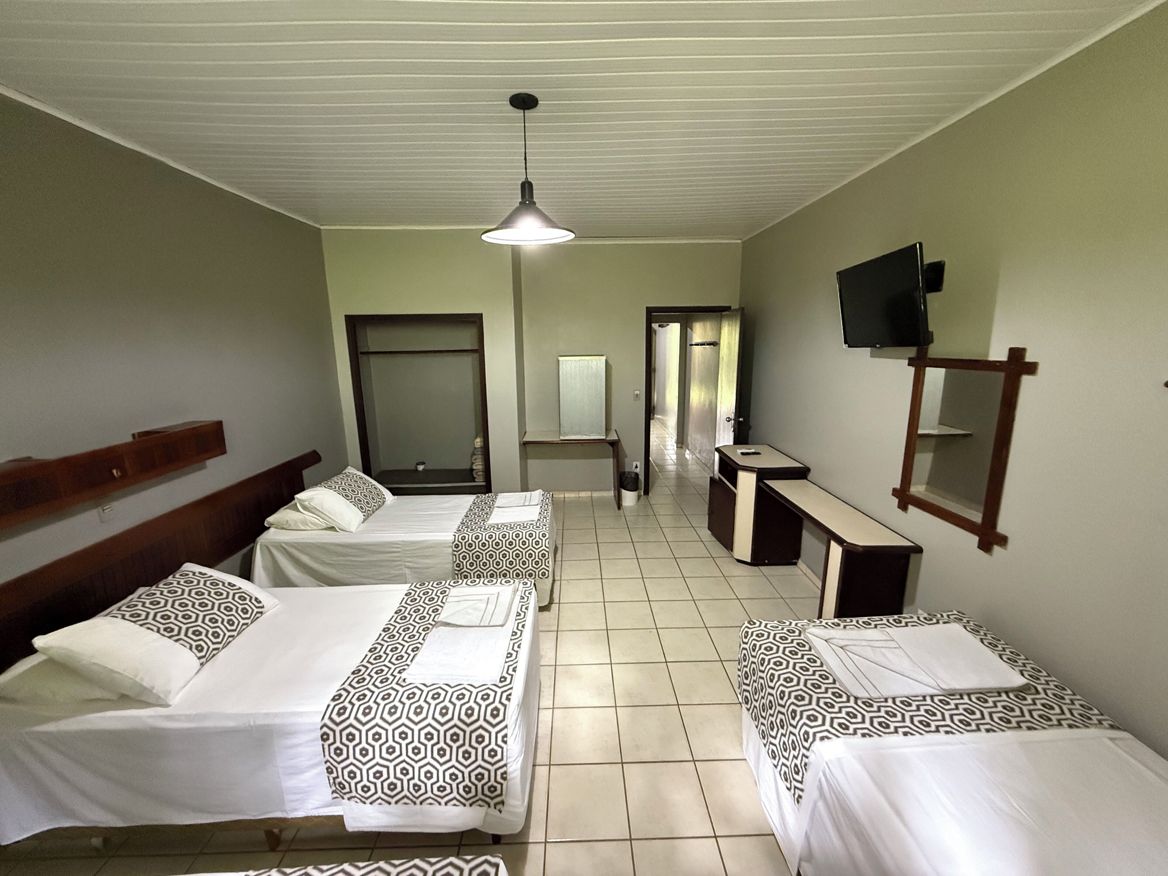 A hotel room with three beds, a desk, a TV, and a mirror.
