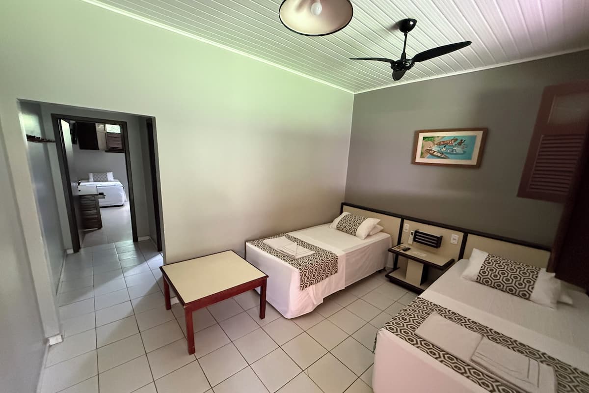 Une chambre d’hôtel avec deux lits simples, une petite table, un ventilateur de plafond et un tableau au mur.