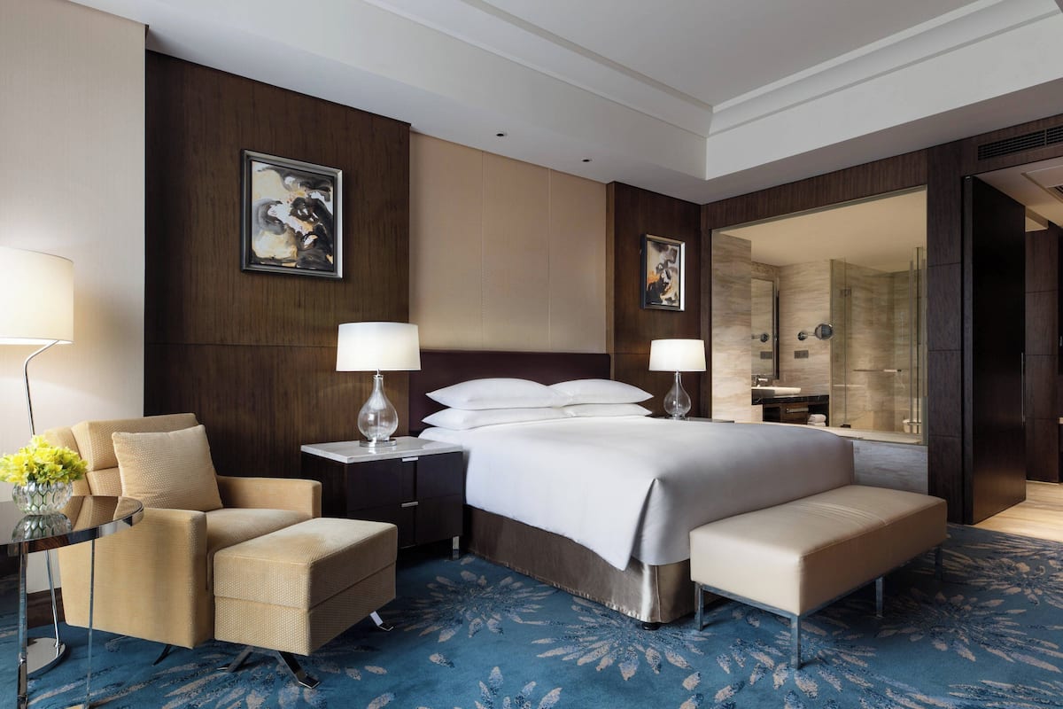 Een hotelkamer met een groot bed, een zithoek met een stoel, een nachtkastje met een lamp en een badkamer die door een open deur zichtbaar is.