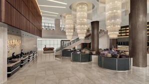 Eine großzügige Lobby mit hohen Decken, modernen Kronleuchtern, einer zentralen Treppe und einem Empfangsbereich mit Sitzgelegenheiten.