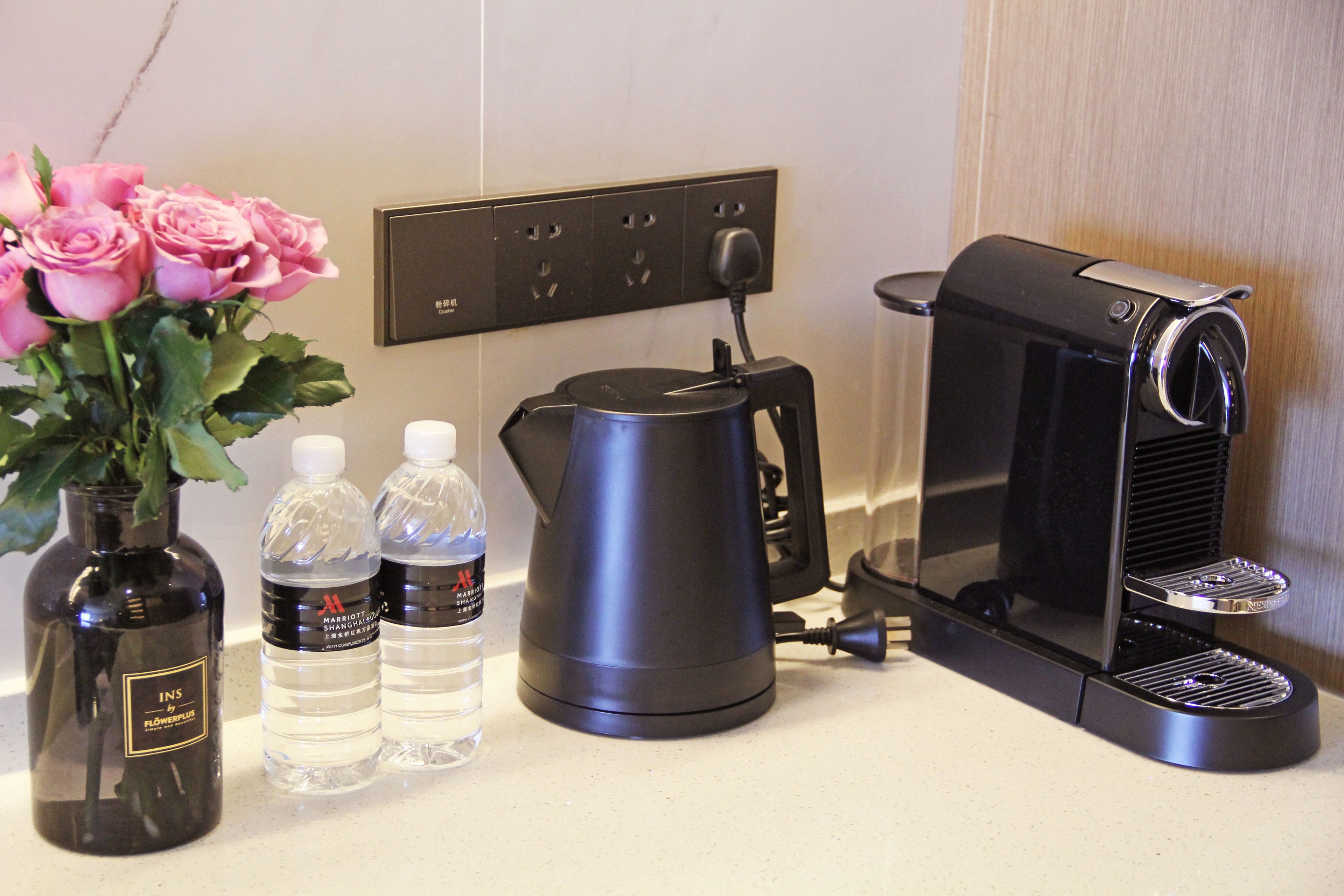A coffee maker, a water dispenser, and a vase with pink roses on a countertop.