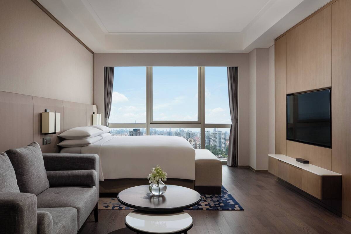 Een moderne hotelkamer met een groot bed, een bank, een televisie en uitzicht over de stad.