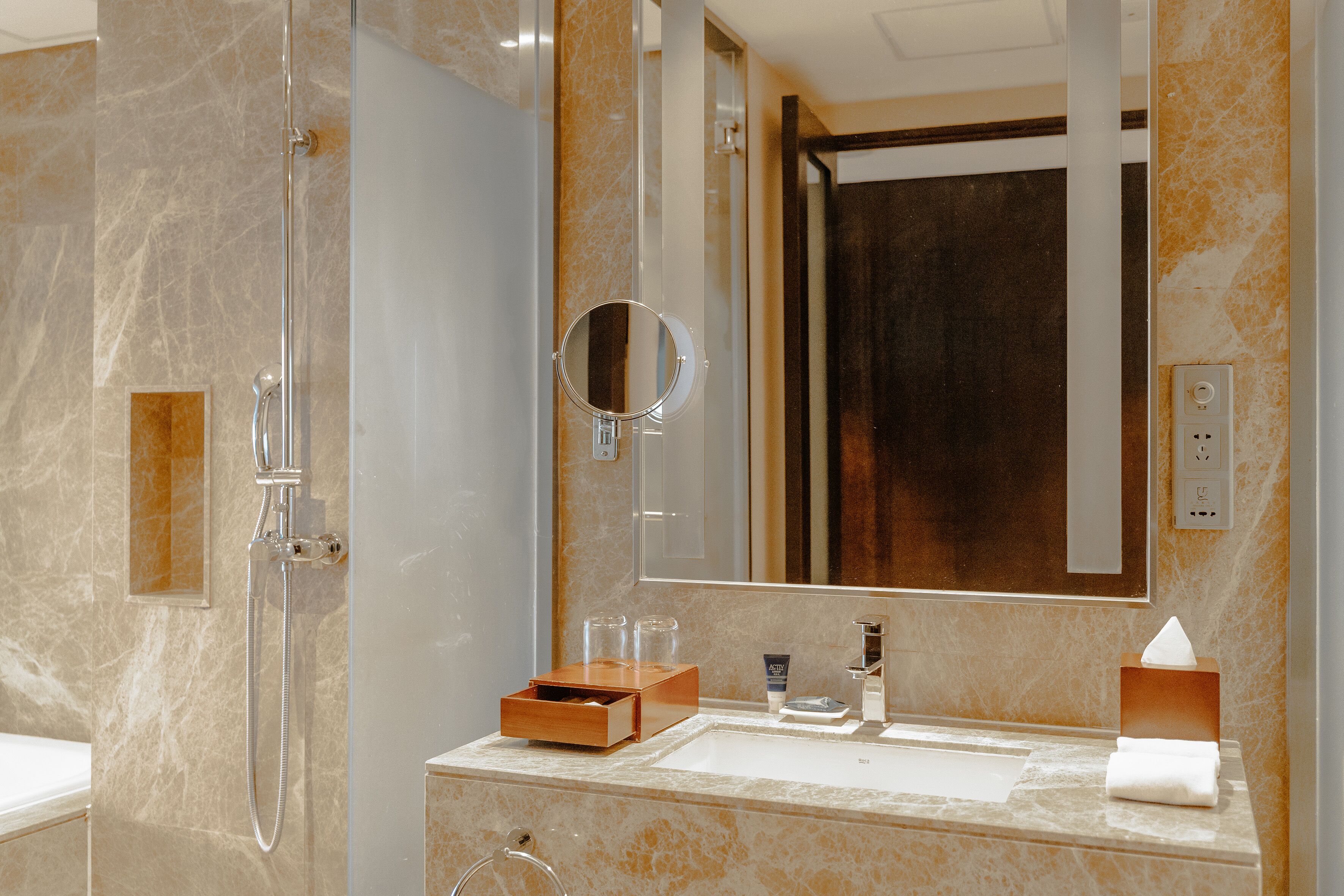 Een moderne badkamer met een douchecabine van glas, een marmeren wastafel en een grote spiegel.