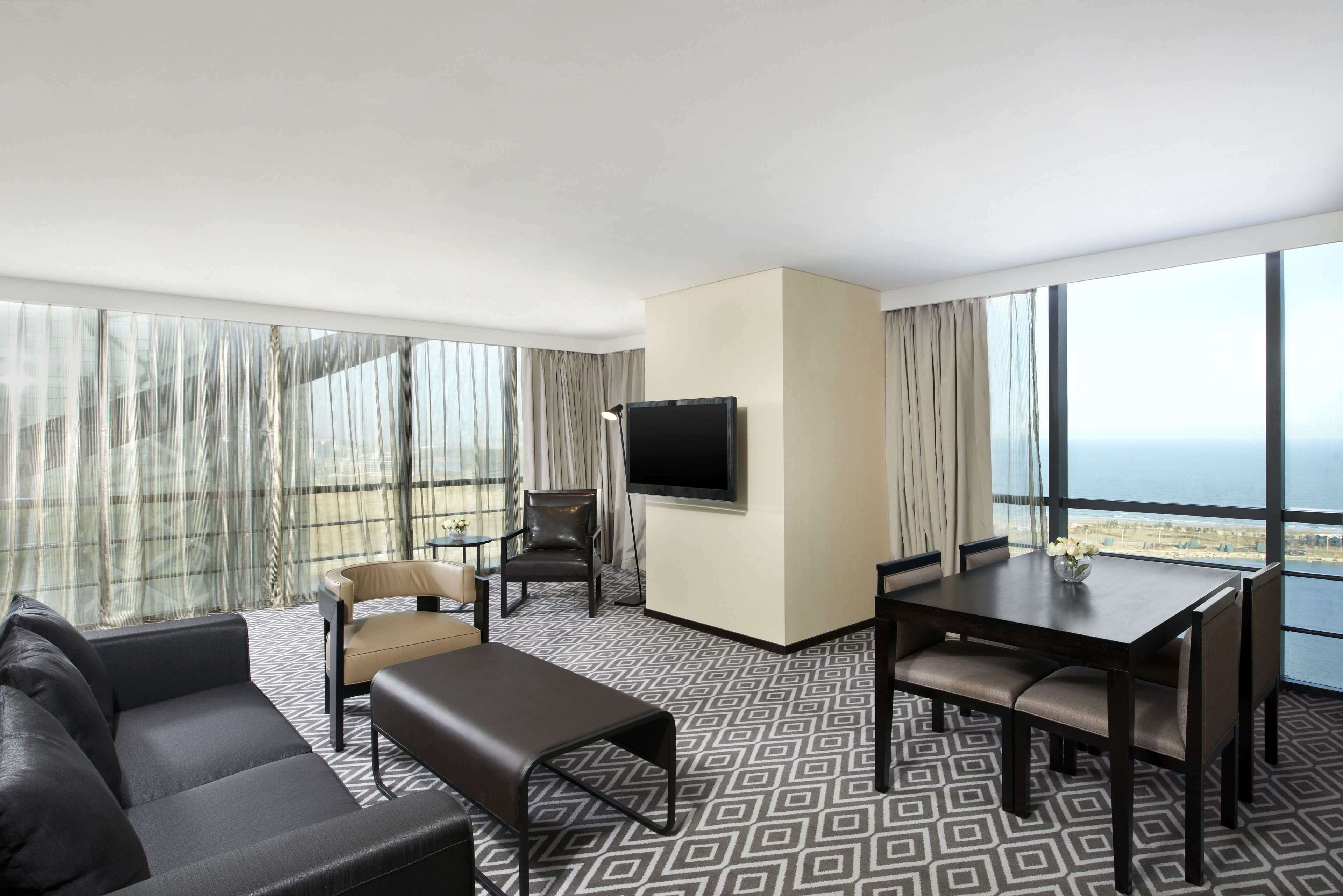 Una habitación de hotel moderna con un ventanal grande, un sofá, una mesa de comedor y un televisor.