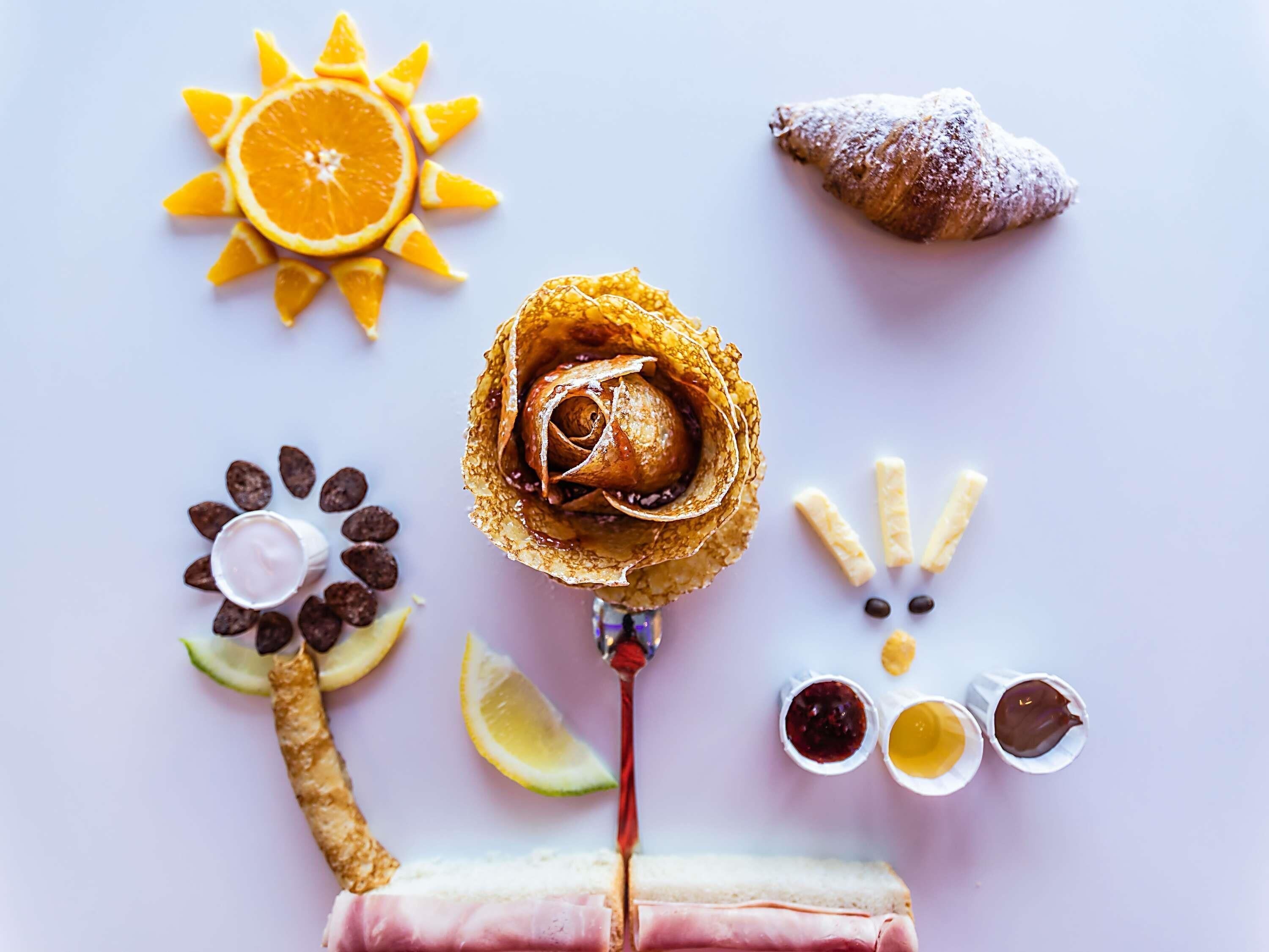 A dessert arrangement with a rose, orange slices, a croissant, chocolate pieces, and a sandwich.