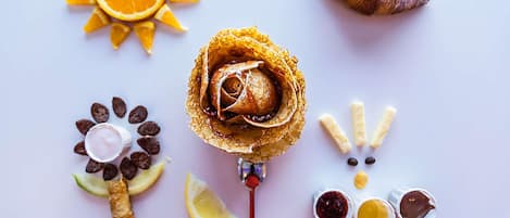 Presentación de postres con una rosa, rodajas de naranja, un croissant, trozos de chocolate y un sándwich.
