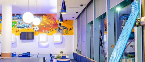 A room with a ping pong table, seating area, and a large window with a view.