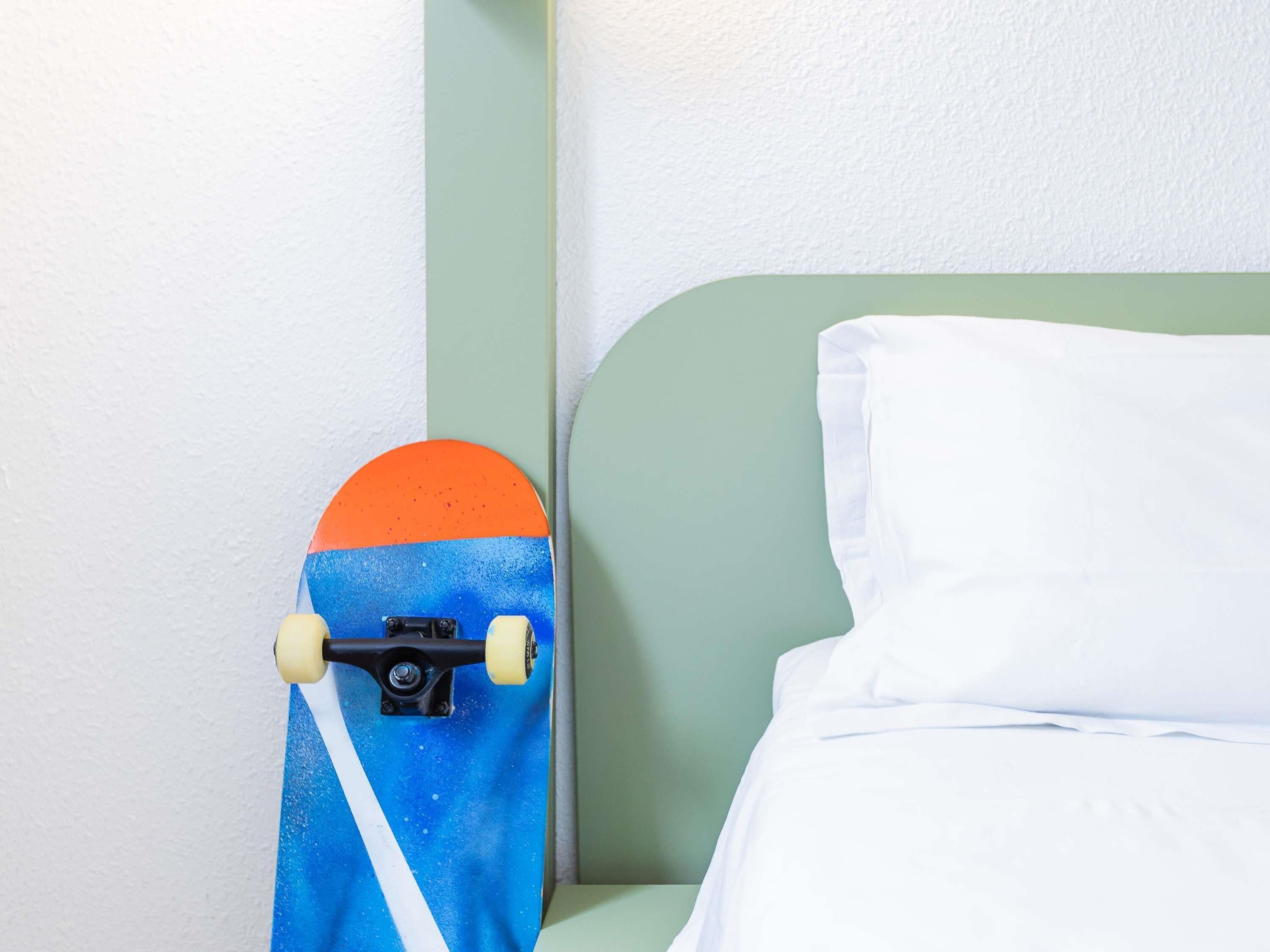 A bed with white sheets and a green headboard, a white pillow, and a skateboard leaning against the wall.