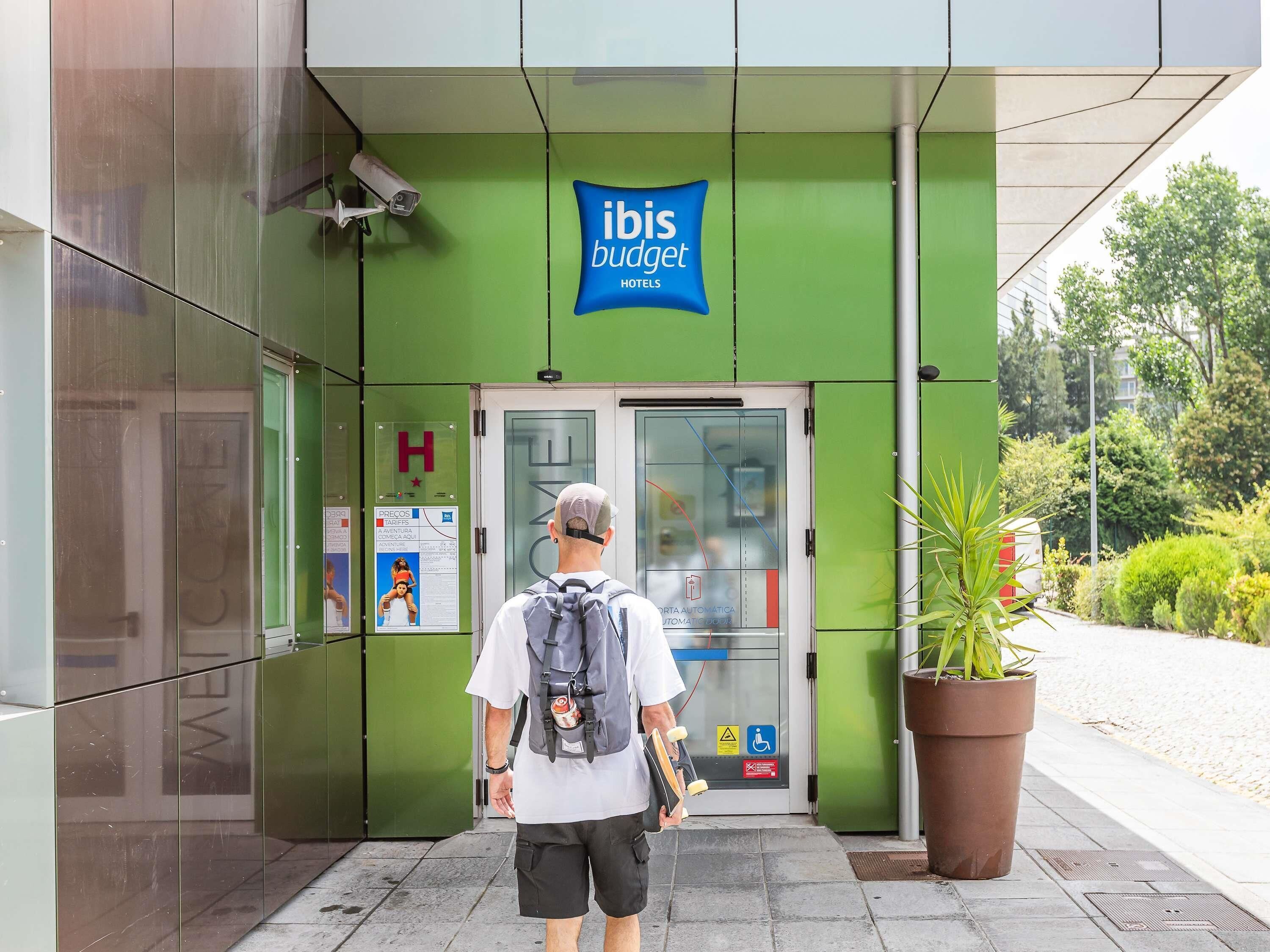 A hotel entrance with a green facade, a sign for 'ibis budget hotels,' and a security camera above the door.