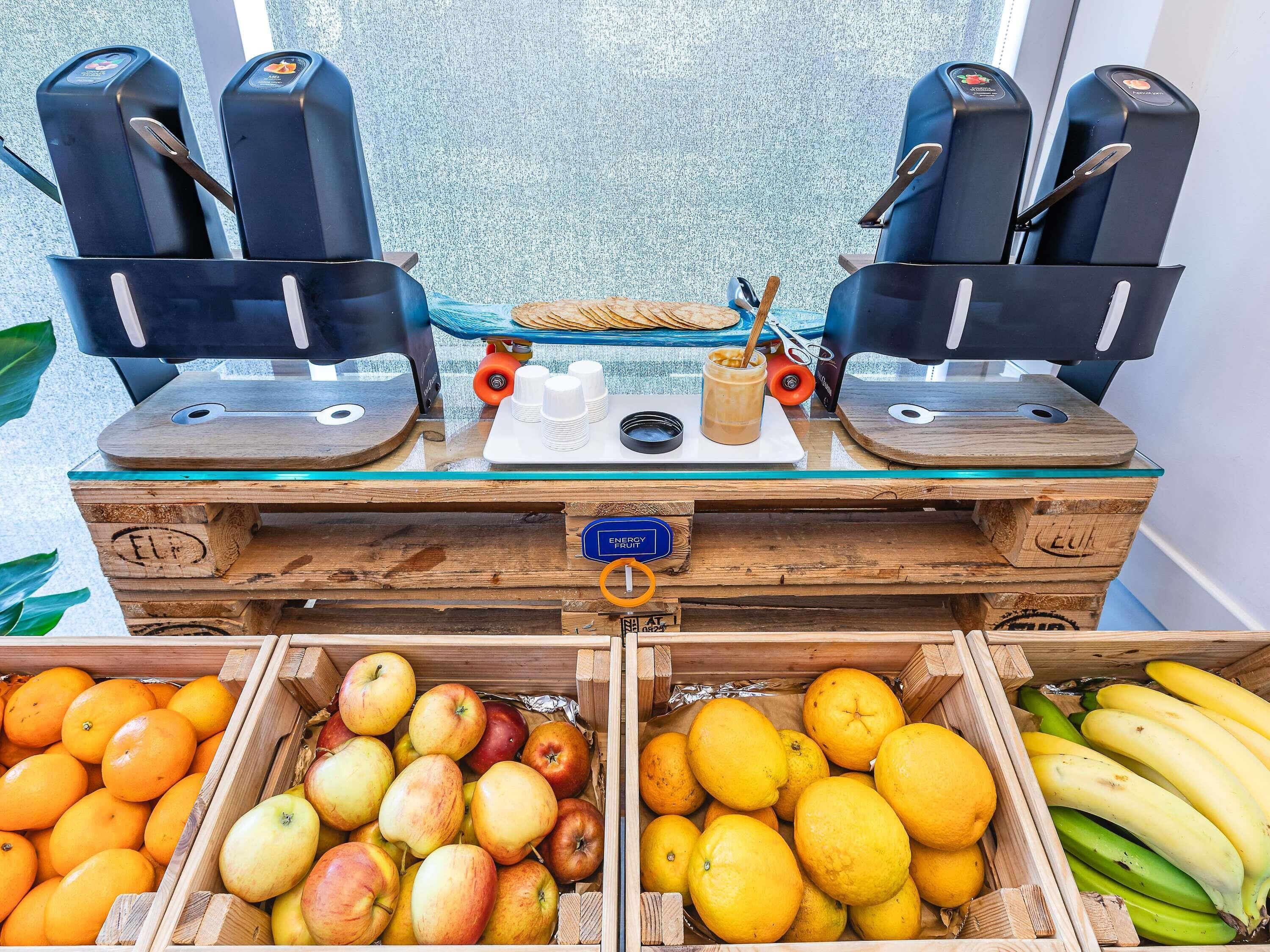 A coffee station with espresso machines, a tray with cups and a drink, and a wooden crate with fruits like apples and oranges.