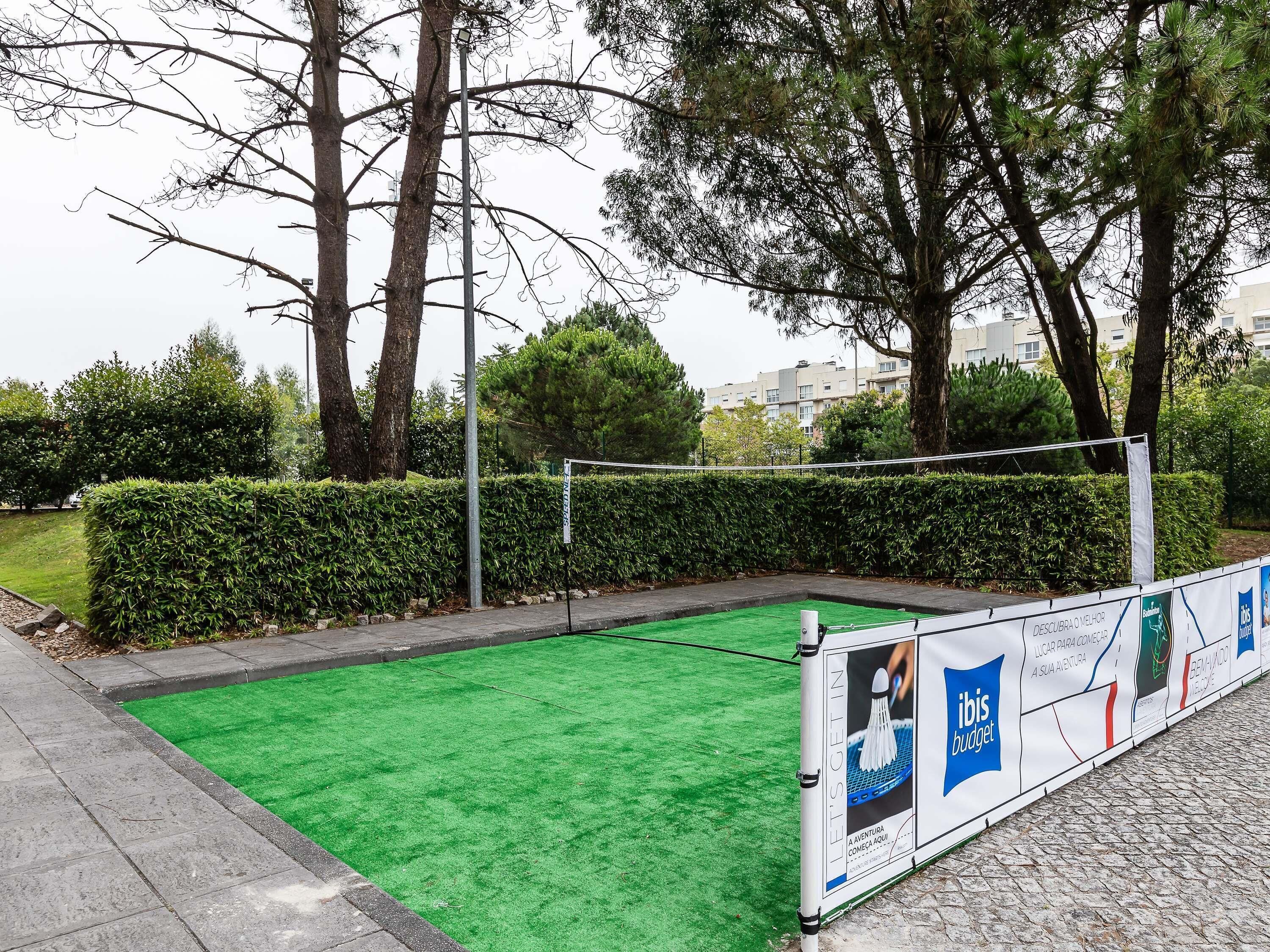 A sports court with a green surface, surrounded by a hedge and trees.