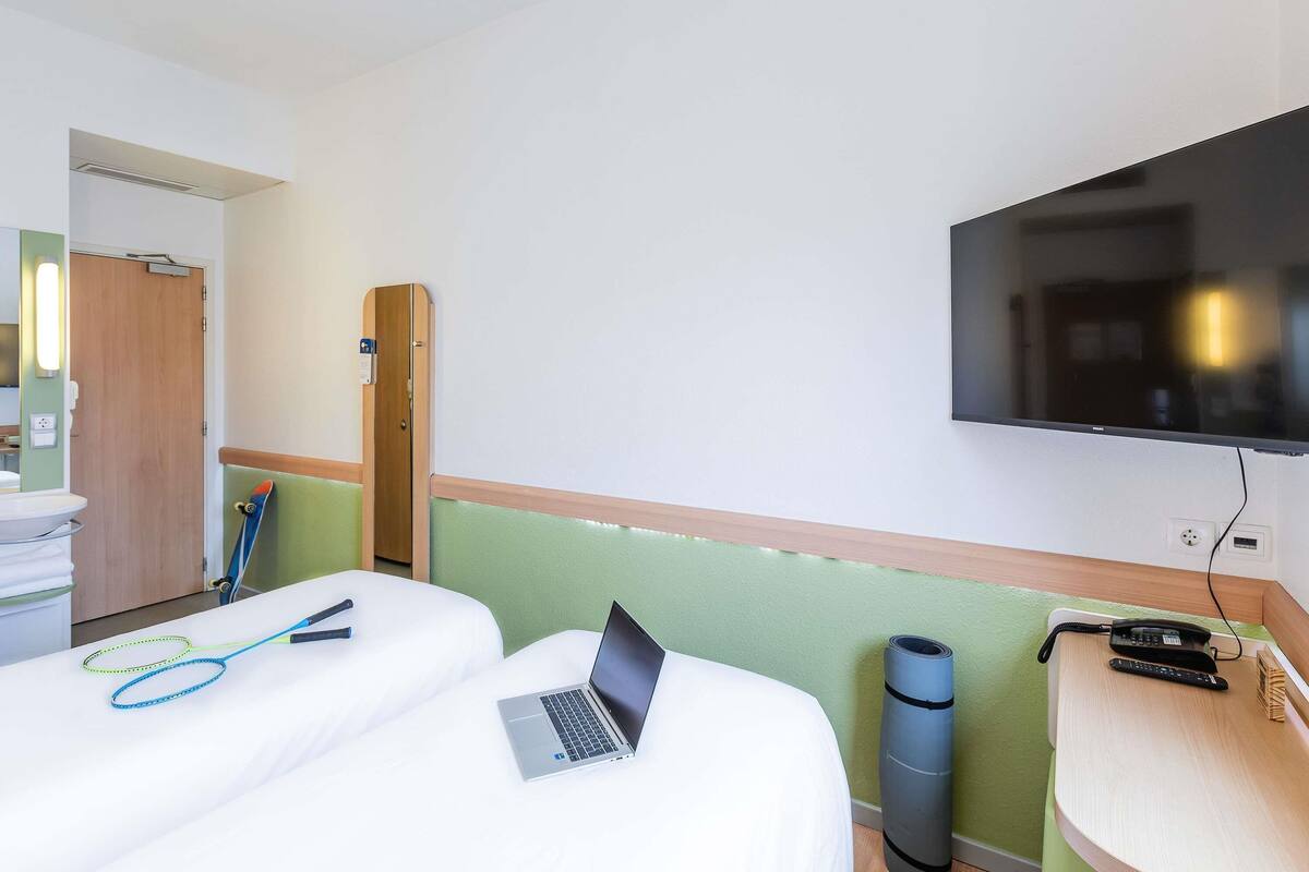 A hotel room with two beds, a laptop, a TV, and a desk with a phone and a trash bin.