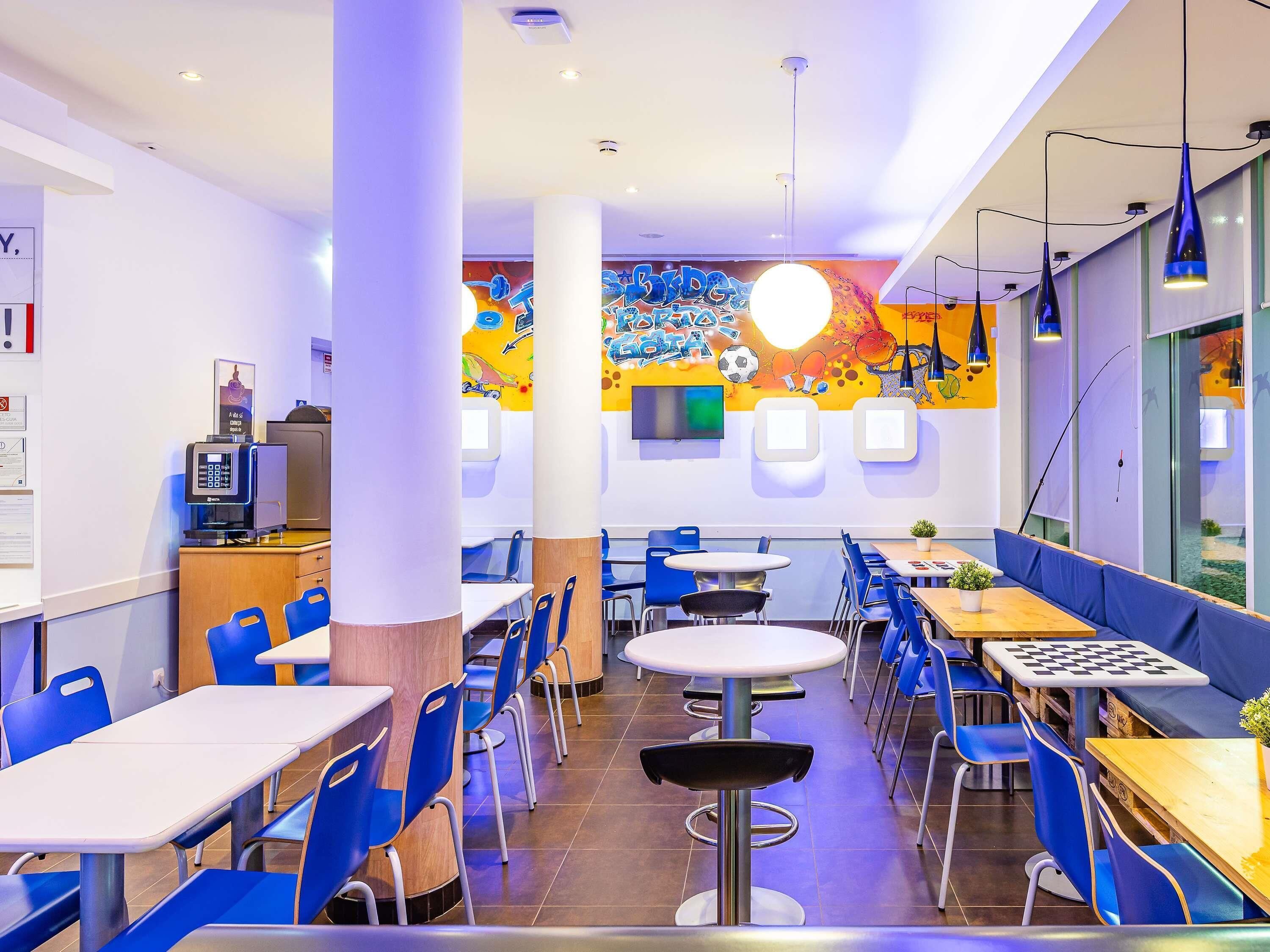 A modern cafeteria with blue chairs, round tables, and a colorful mural on the wall.