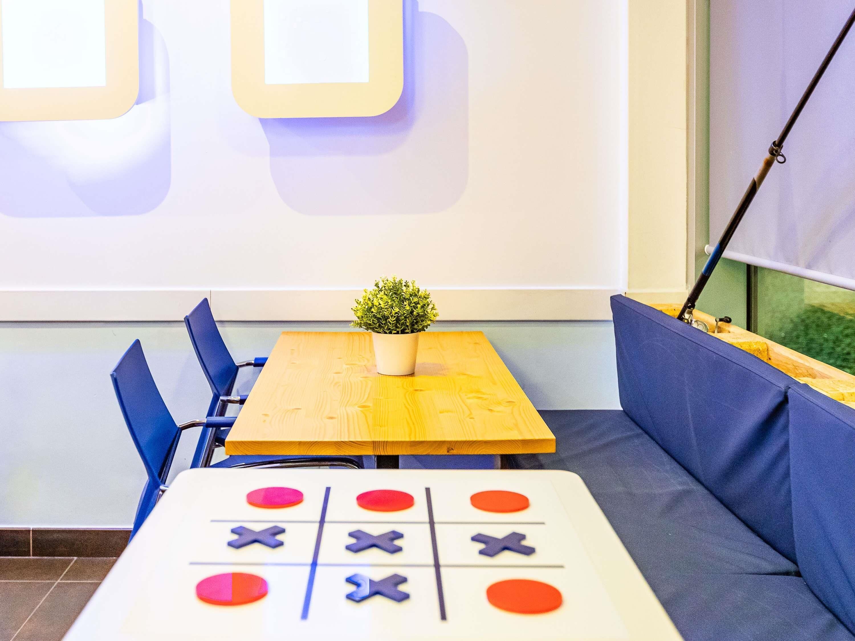 Een kamer met een houten tafel, blauwe stoelen, een kleine potplant en een kruisje-tik-tik-tik spel.