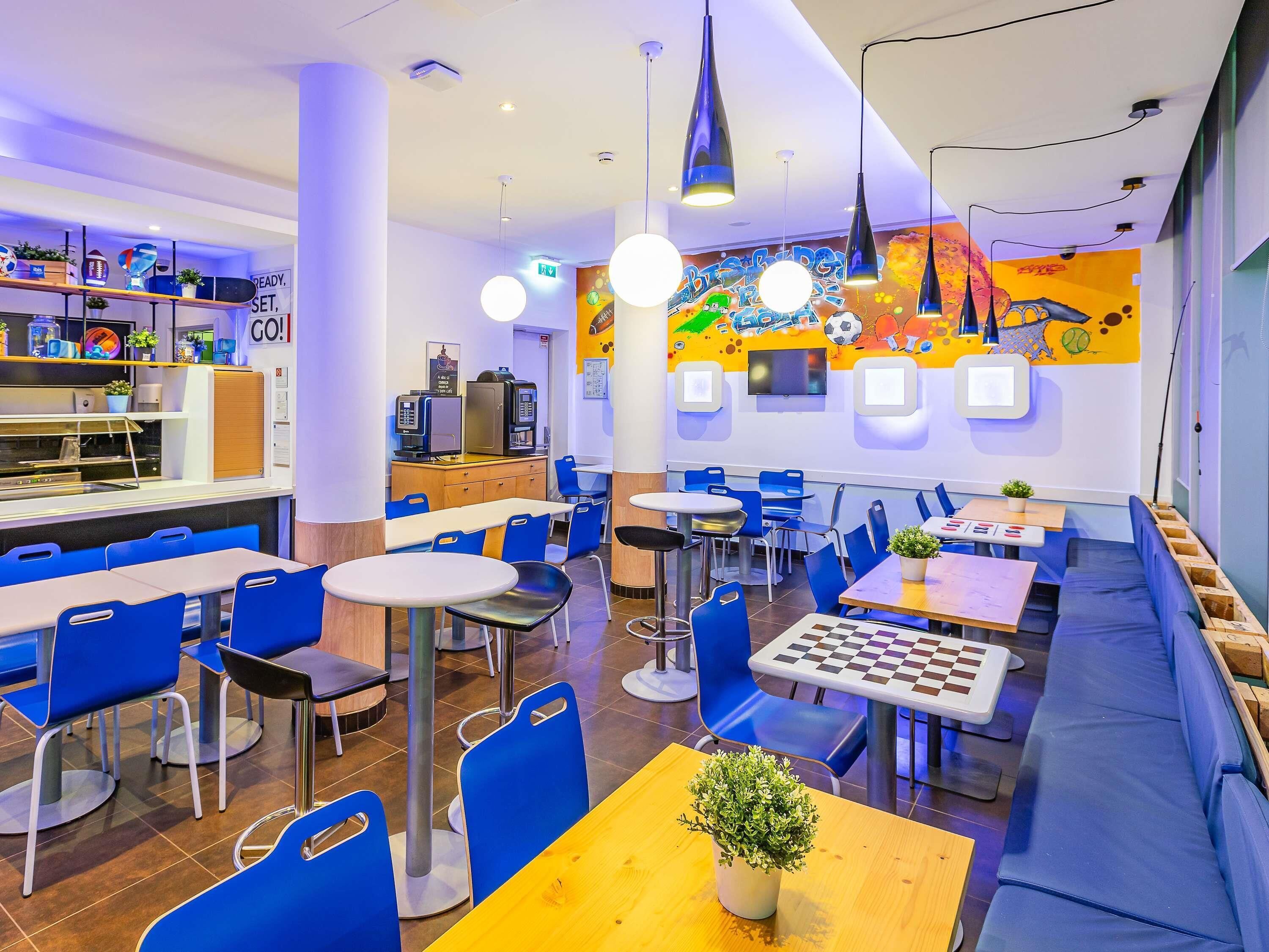 Ein modernes Restaurant mit blauer und weißer Einrichtung, einem Schachbrett und einem farbenfrohen Wandgemälde.