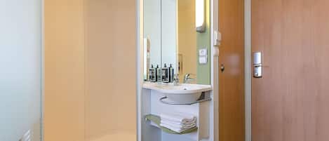 A modern bathroom with a glass shower enclosure, a sink with toiletries, and a wooden door.