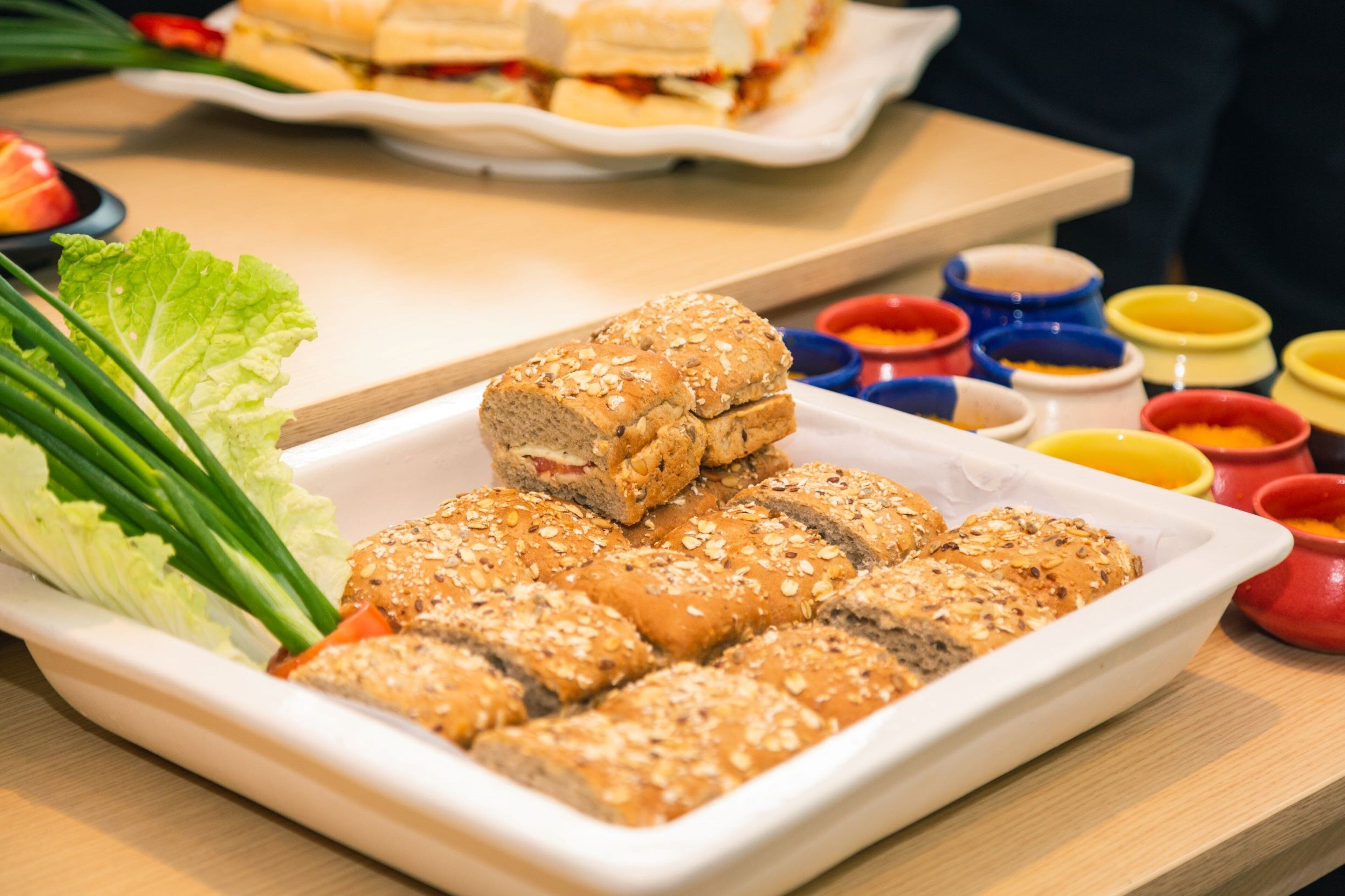 Un plato rectangular blanco con pan en rodajas cubierto de semillas, acompañado de una guarnición de lechuga y cebollas verdes.