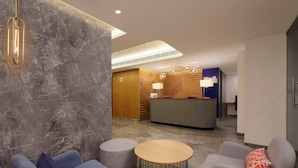 En moderne lobby med marmorvægge, en receptionsdisk, siddeområde med sofaer og et rundt bord, samt et loft med indbygget belysning.