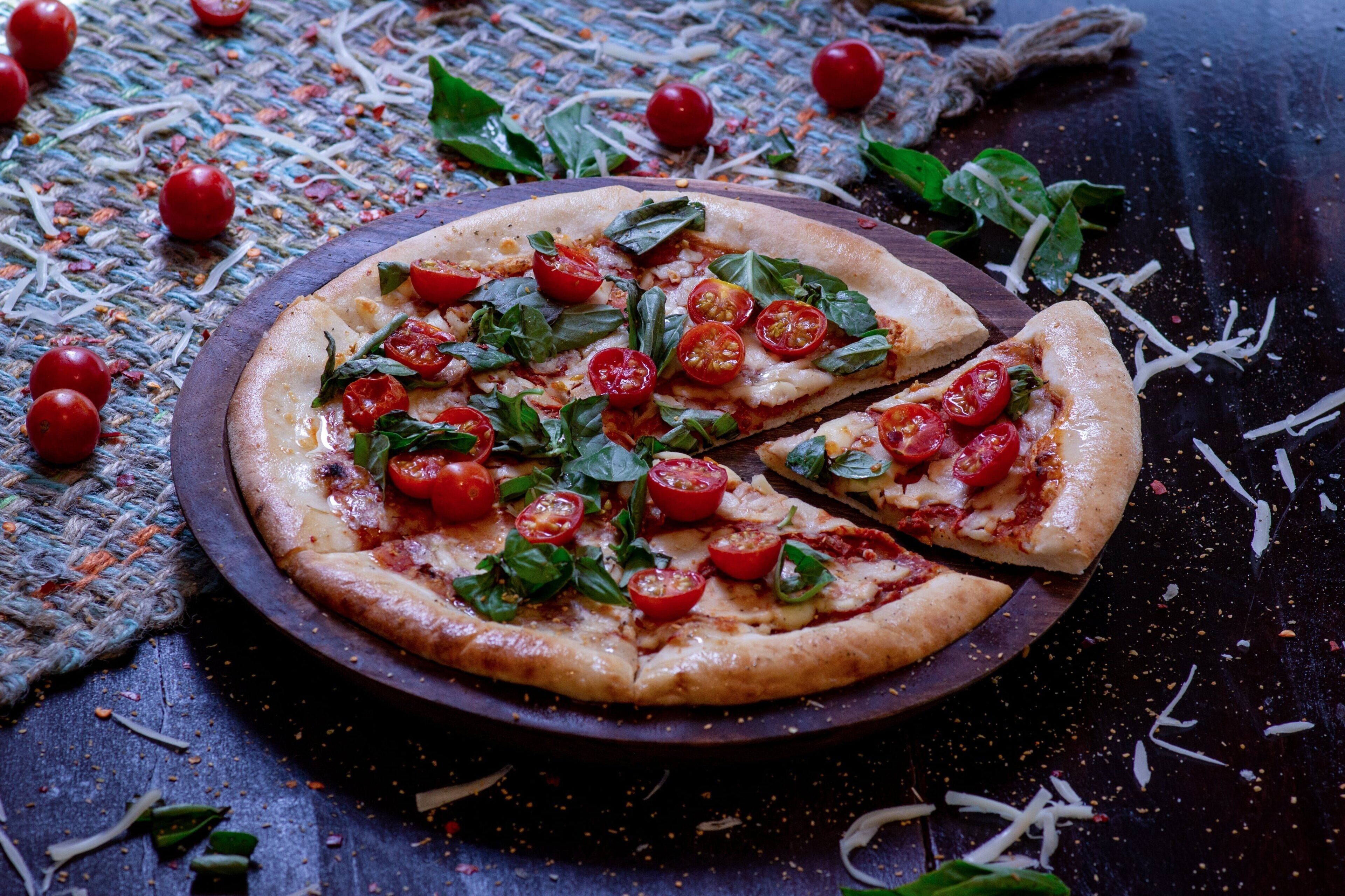 A pizza with tomato and basil toppings on a round wooden board.
