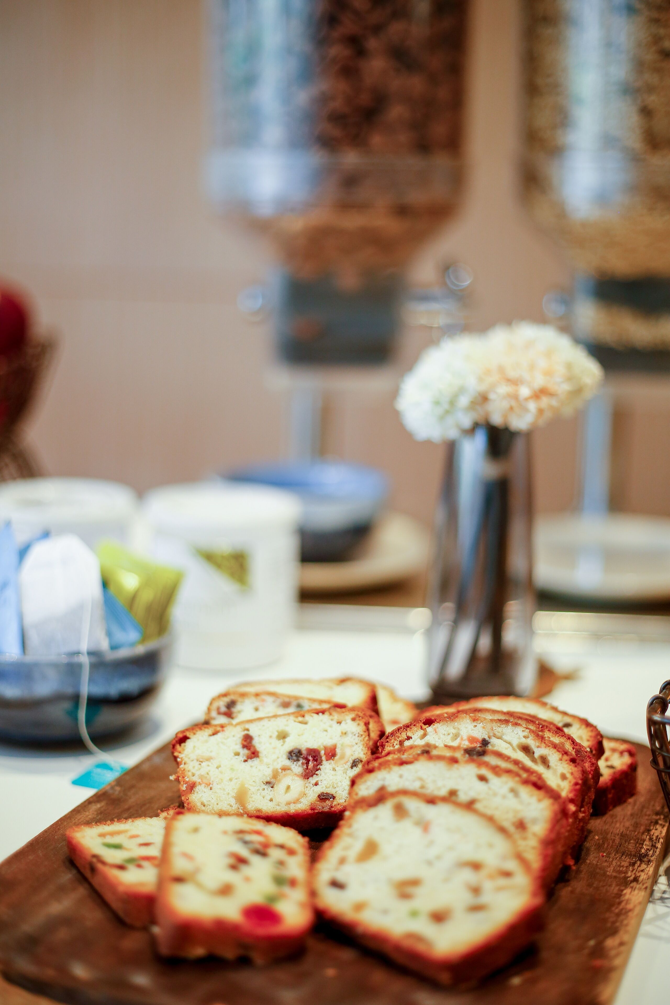 A wooden board with sliced bread and a small vase with white flowers.