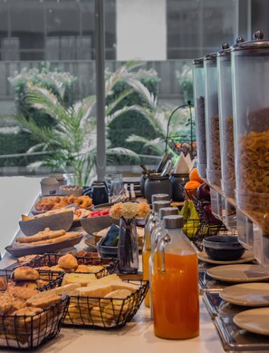 A buffet with various food items and beverages, including bread, pastries, and a juice dispenser. - Holiday Inn Express Ahmdabad Prahlad Nagar by IHG (Ahmedabad)