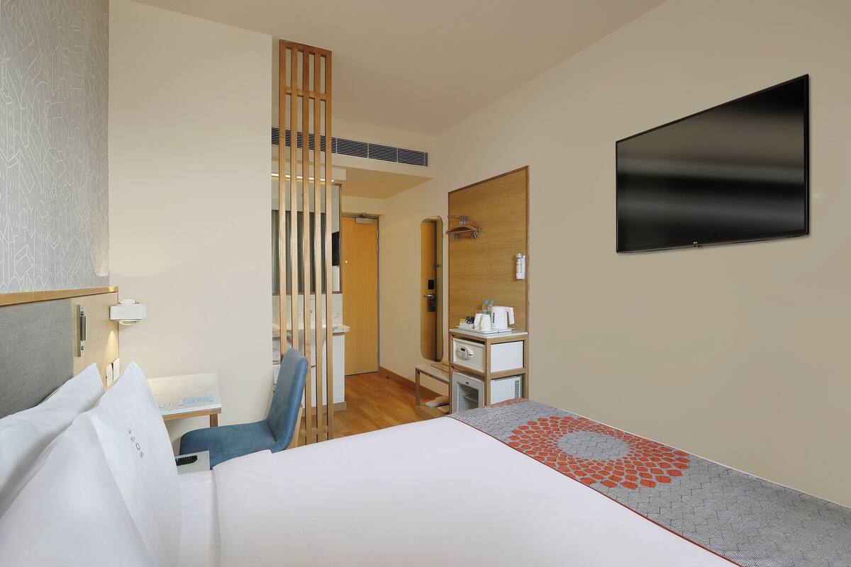 A hotel room with a bed, a desk, a chair, a TV, a mirror, and a wardrobe.