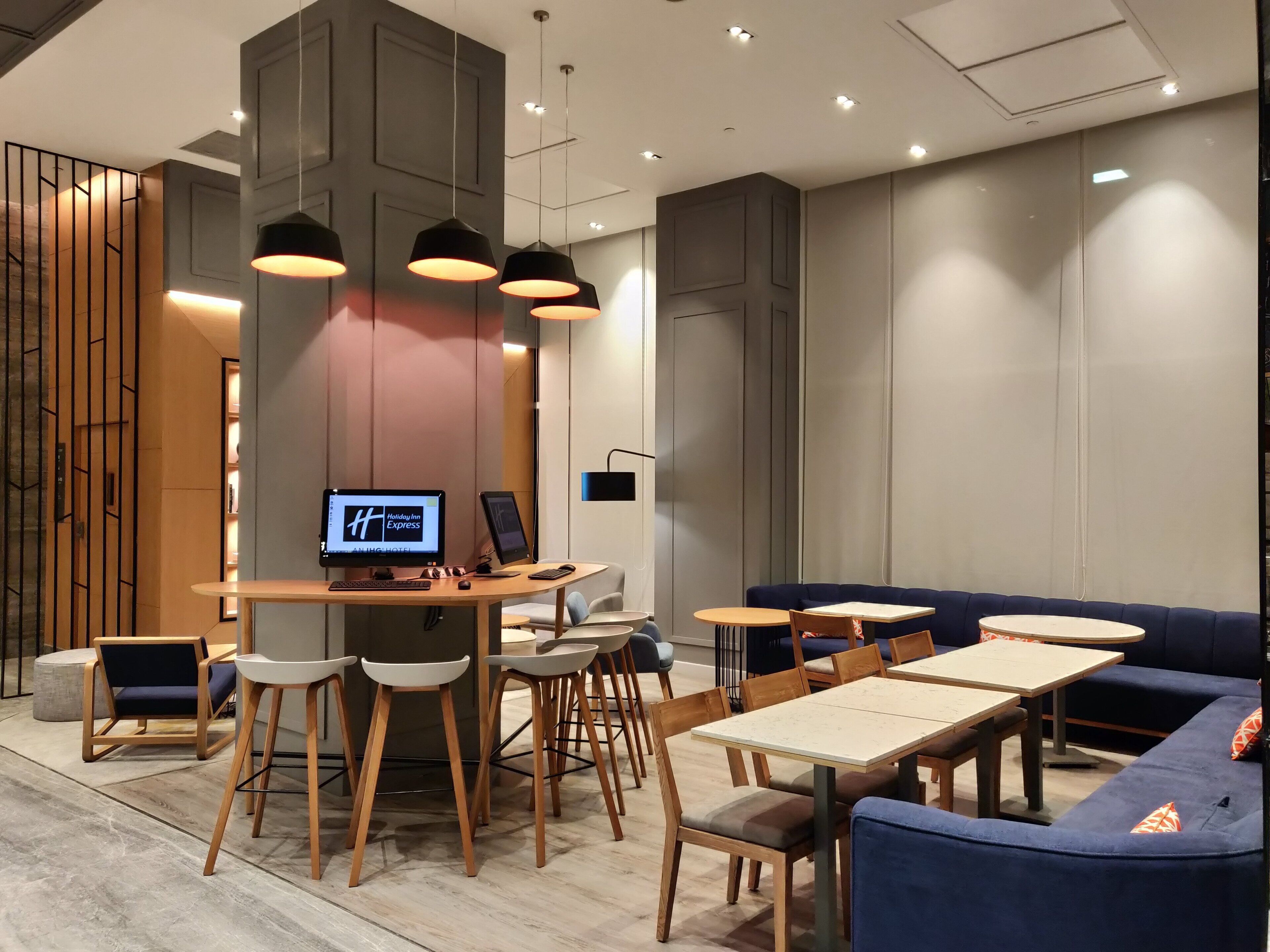 A modern hotel lobby with a reception desk, seating area, and a large screen displaying the hotel's name.