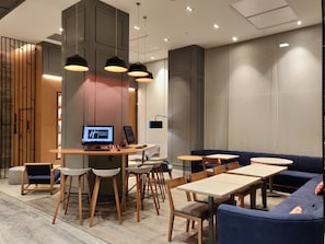 En moderne hotellobby med receptionsdisk, siddeområde og et stort skærm, der viser hotellets navn.