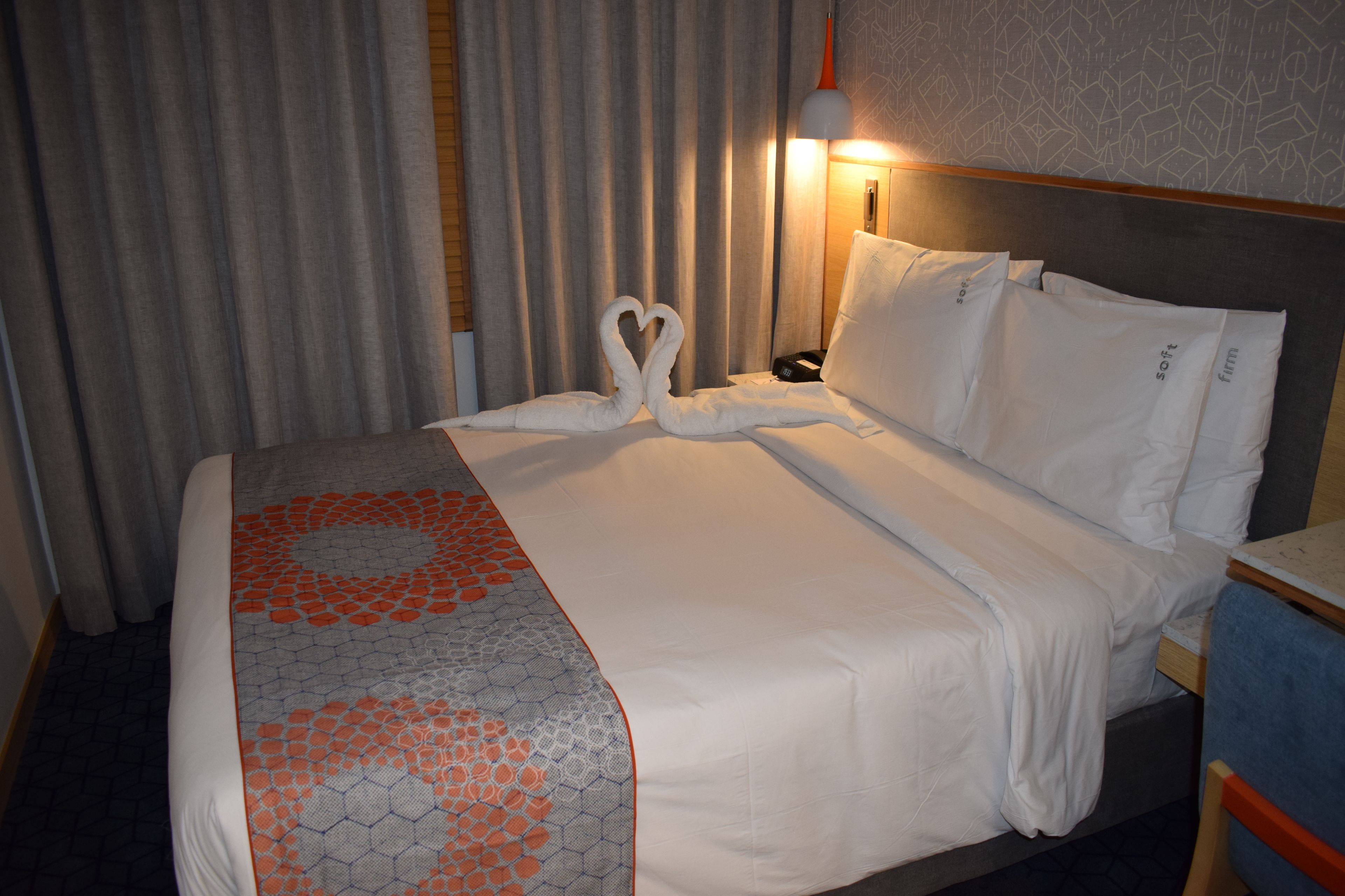 A hotel room with a neatly made bed, a headboard, and a bedside table with a lamp.