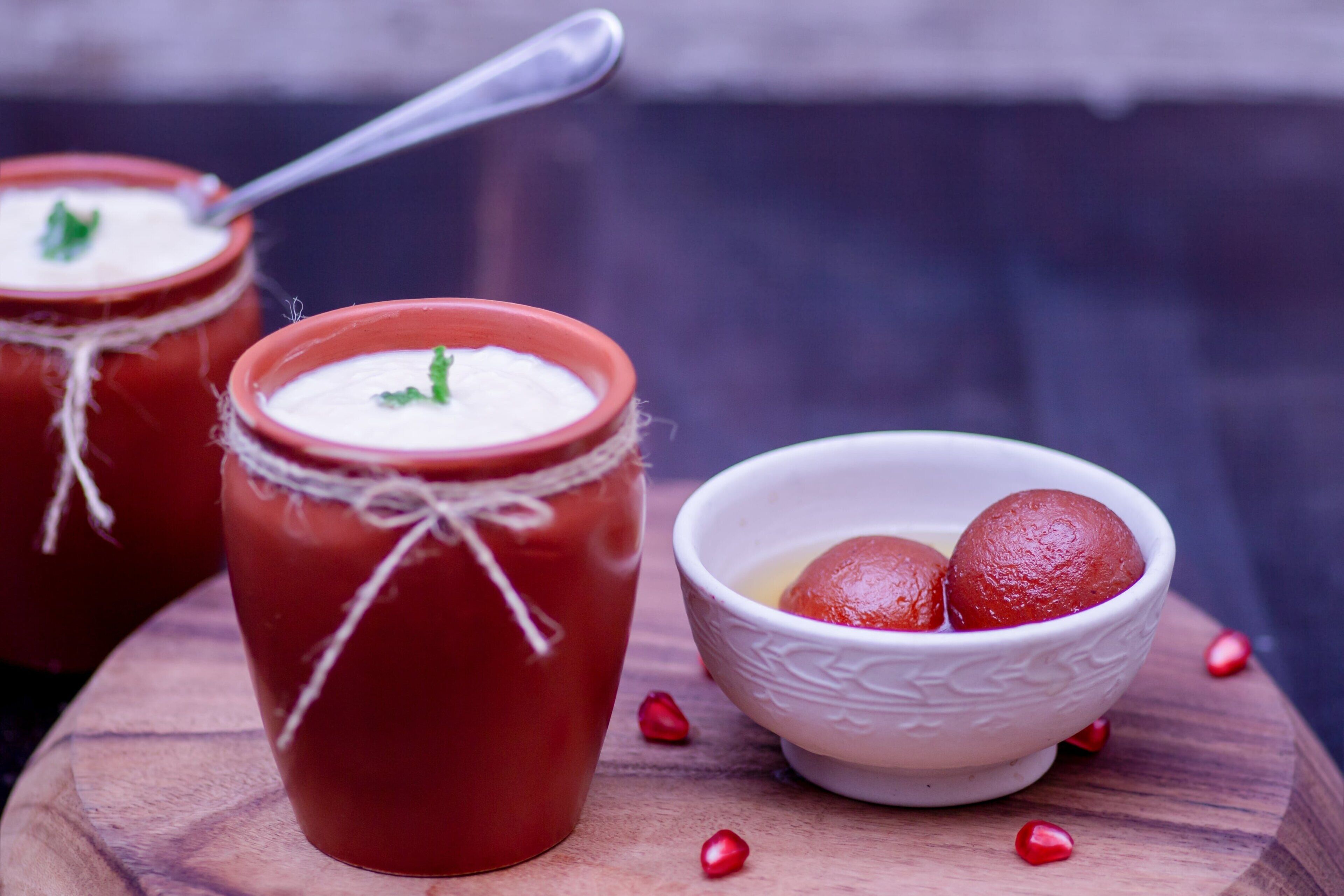 Two red clay pots with white cream and a white bowl containing red sweets on a wooden surface.