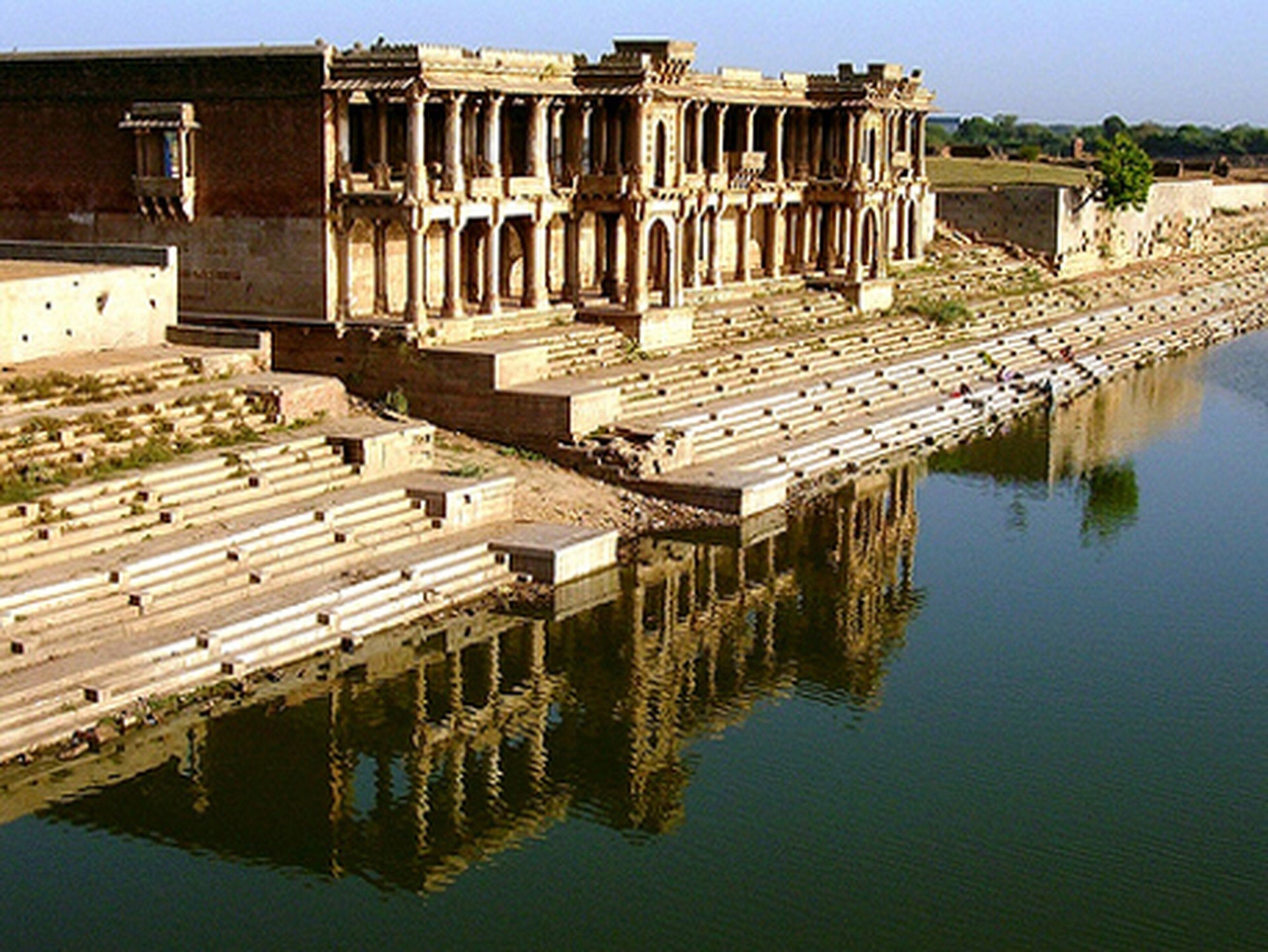 Un bâtiment historique qui se reflète dans l’eau, avec une série de marches menant à son entrée.