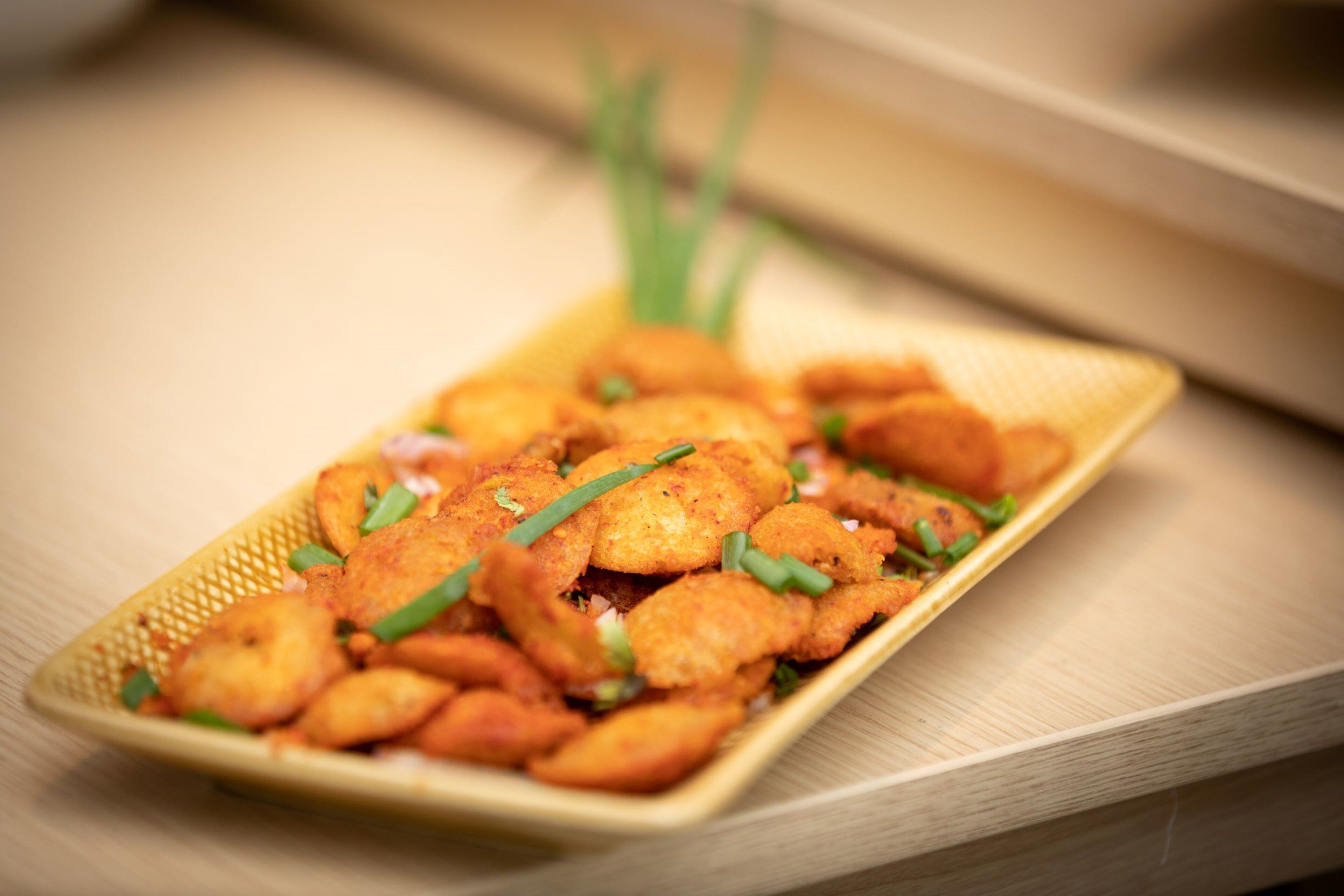 Un plato rectangular con alimentos fritos, adornado con hierbas verdes.