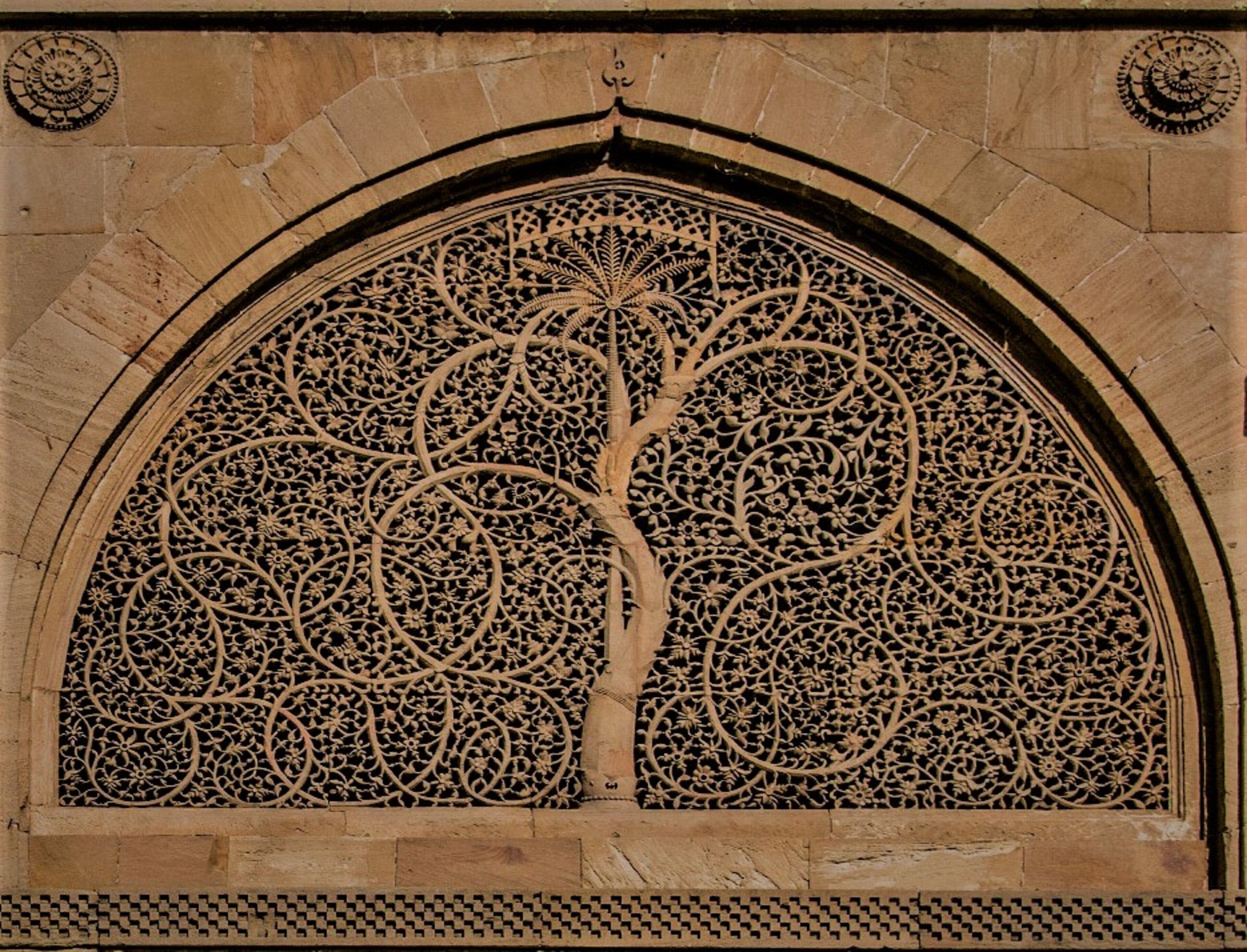 A detailed carved tree design within an arched window.