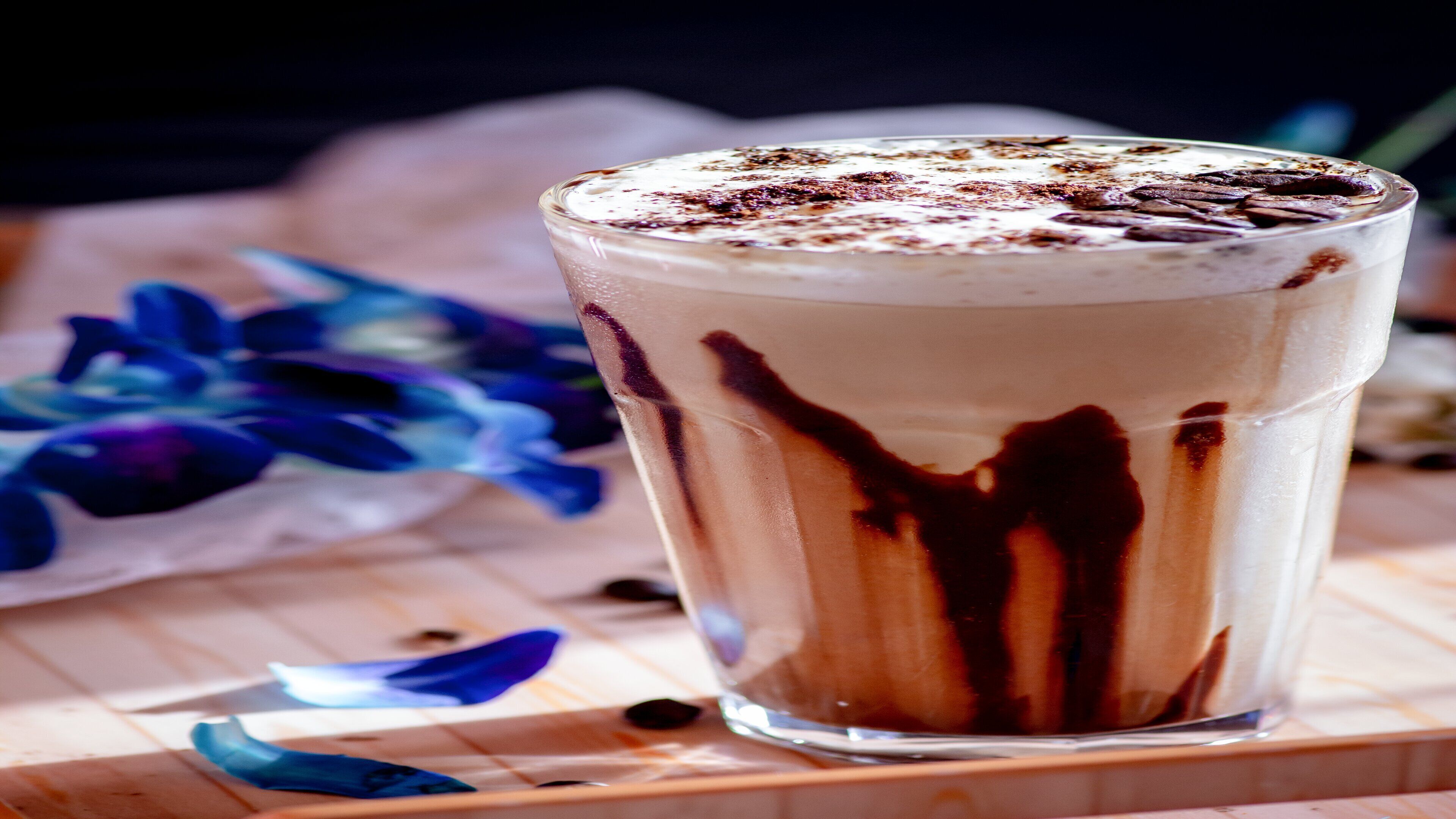 A tall glass of layered beverage with chocolate drizzle on a wooden surface.